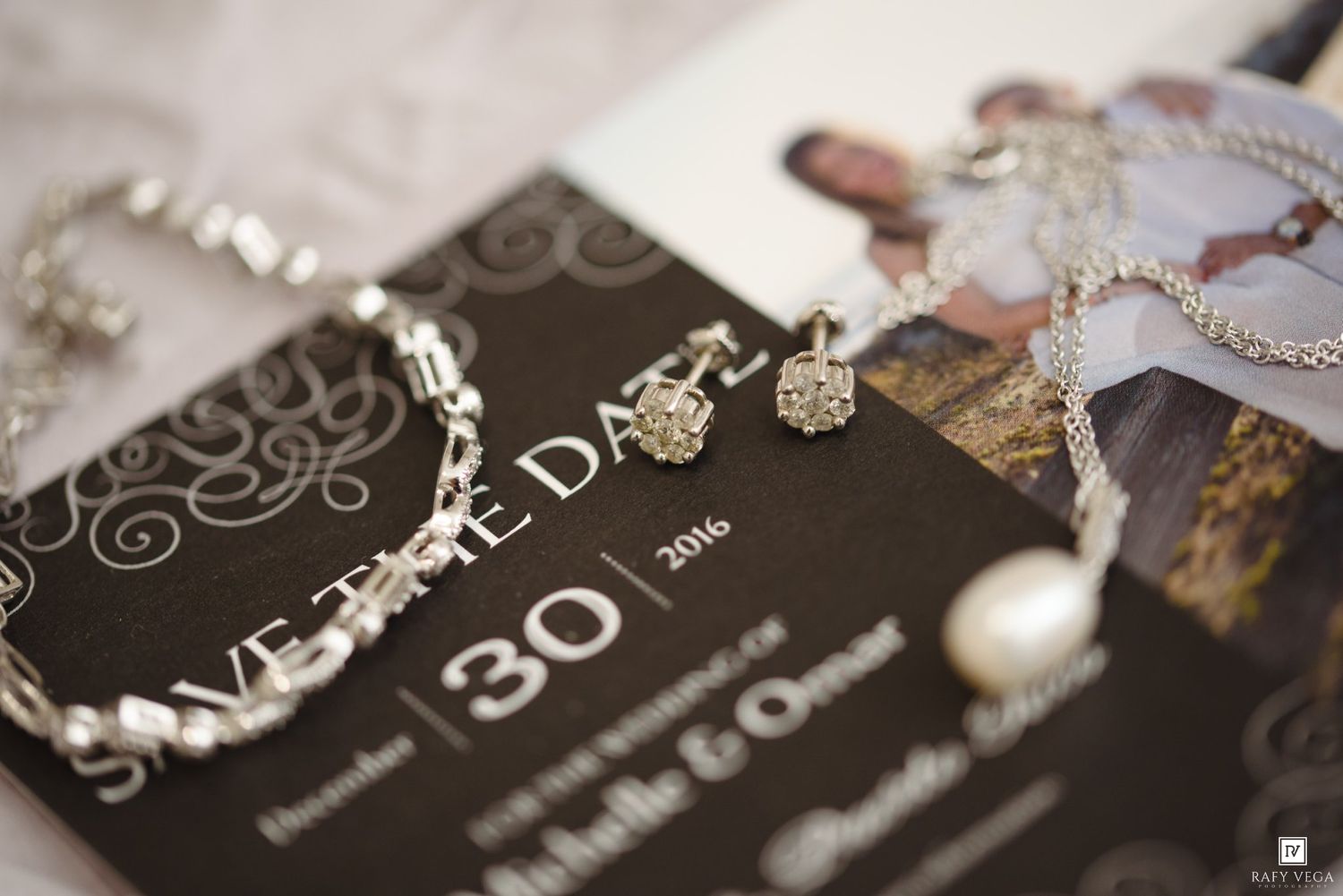 Elegant wedding save the date card with silver jewelry, bracelet, earrings, and necklace displayed on a dark background.