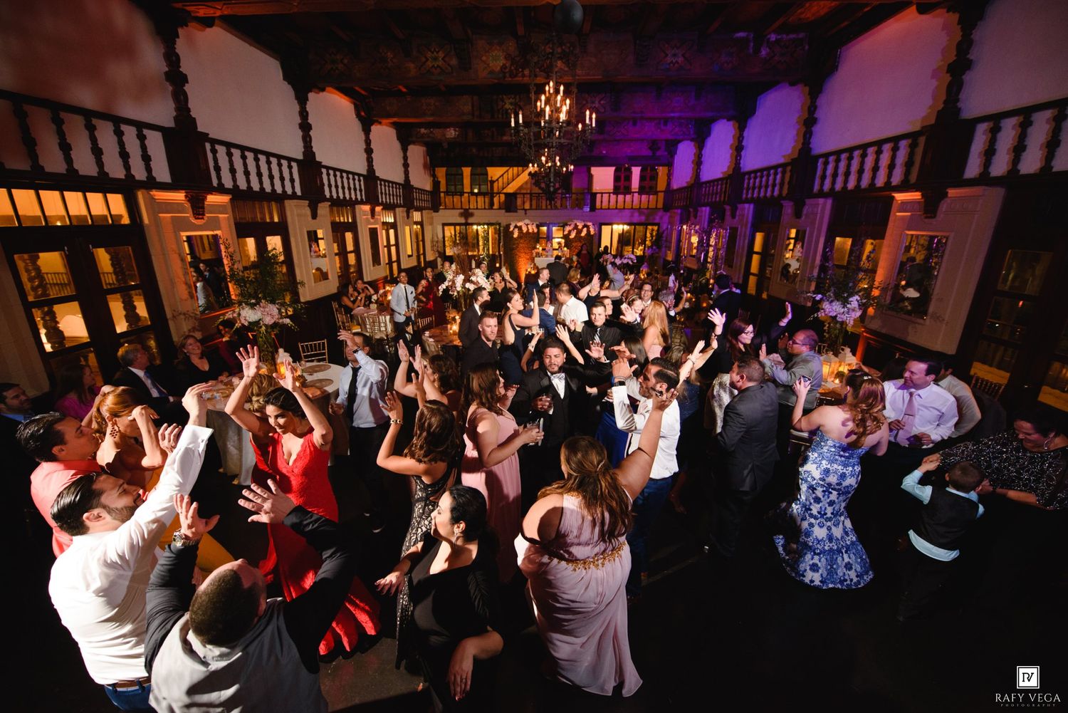 Aerial view of a large wedding reception dance floor packed with guests dancing under warm chandelier lighting.
