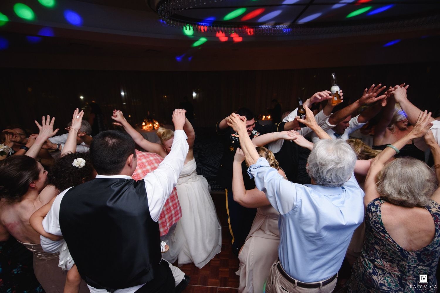 Joyful wedding reception dance floor with guests raising hands under colorful disco lights.