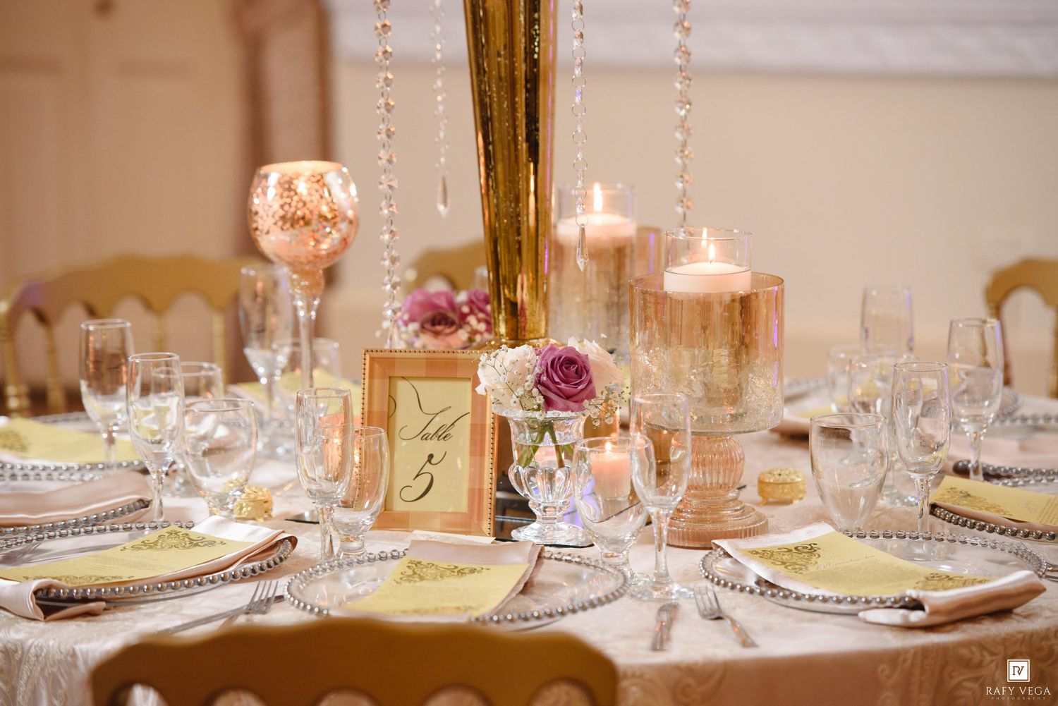 Elegant wedding reception table with gold centerpiece, candles, crystal garlands, and floral arrangements.
