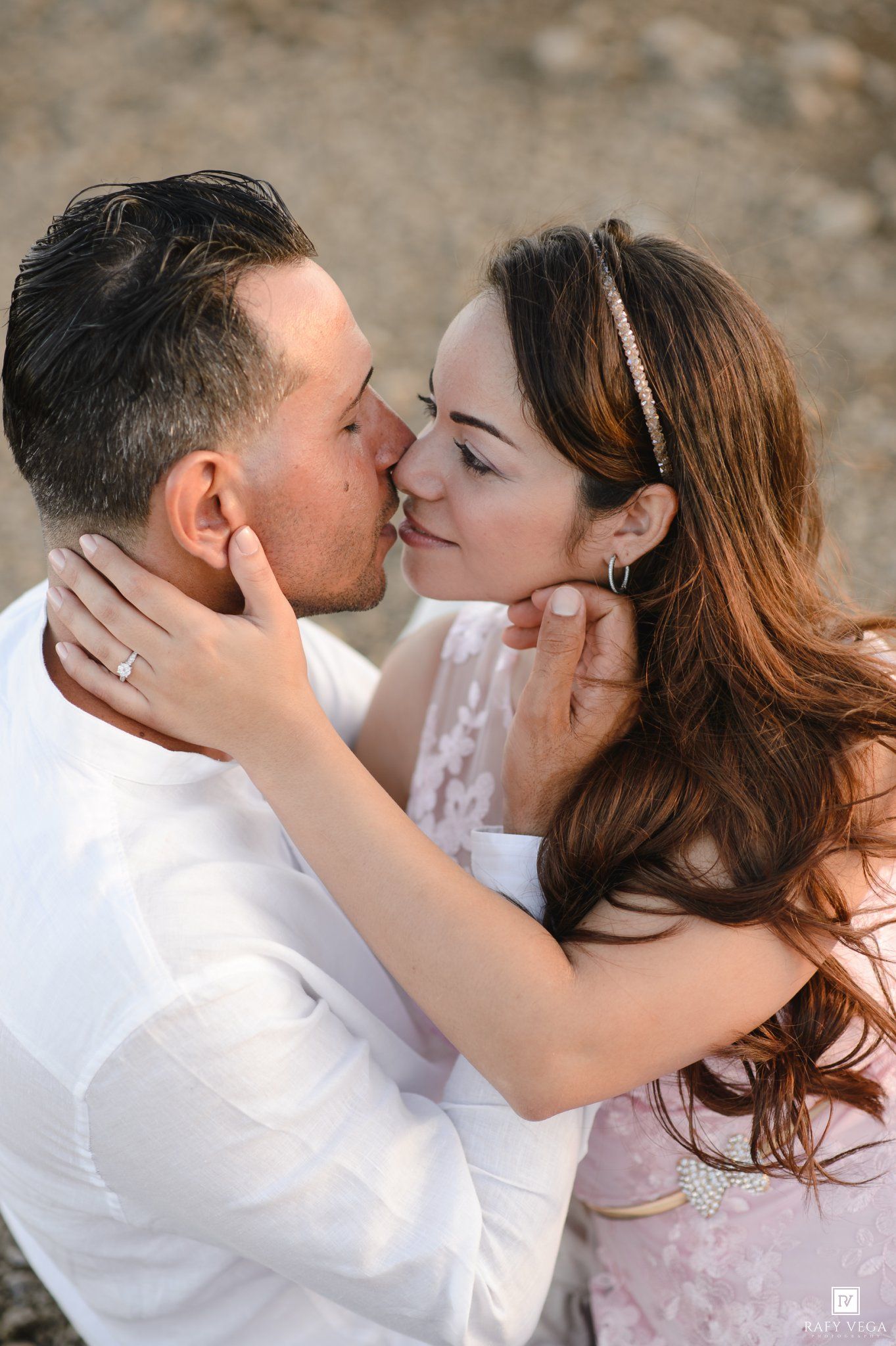 Couple sharing a romantic kiss during engagement photo session, woman wearing pink lace dress and crystal headband.