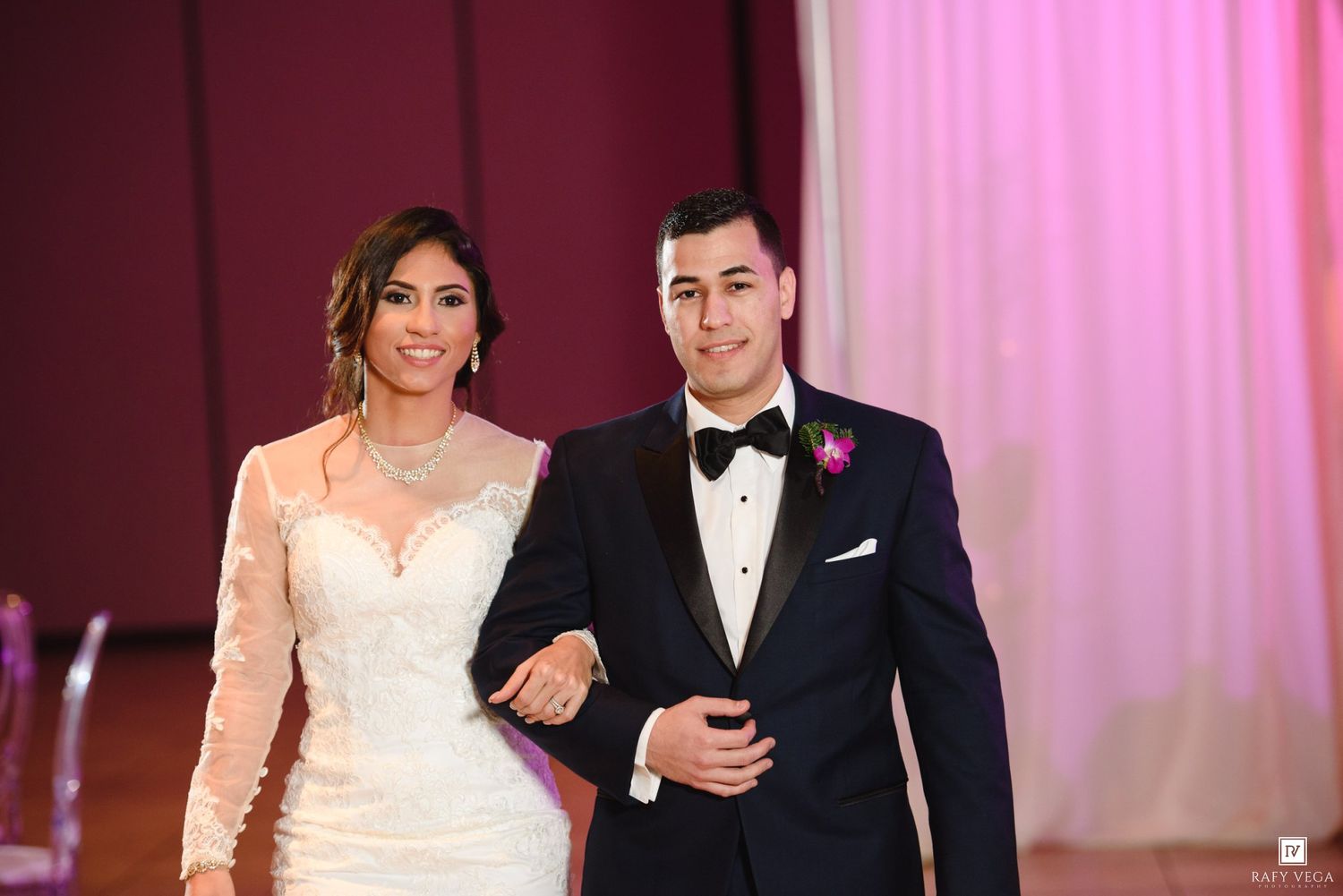 Bride in lace wedding gown and groom in navy tuxedo smile during wedding reception grand entrance.