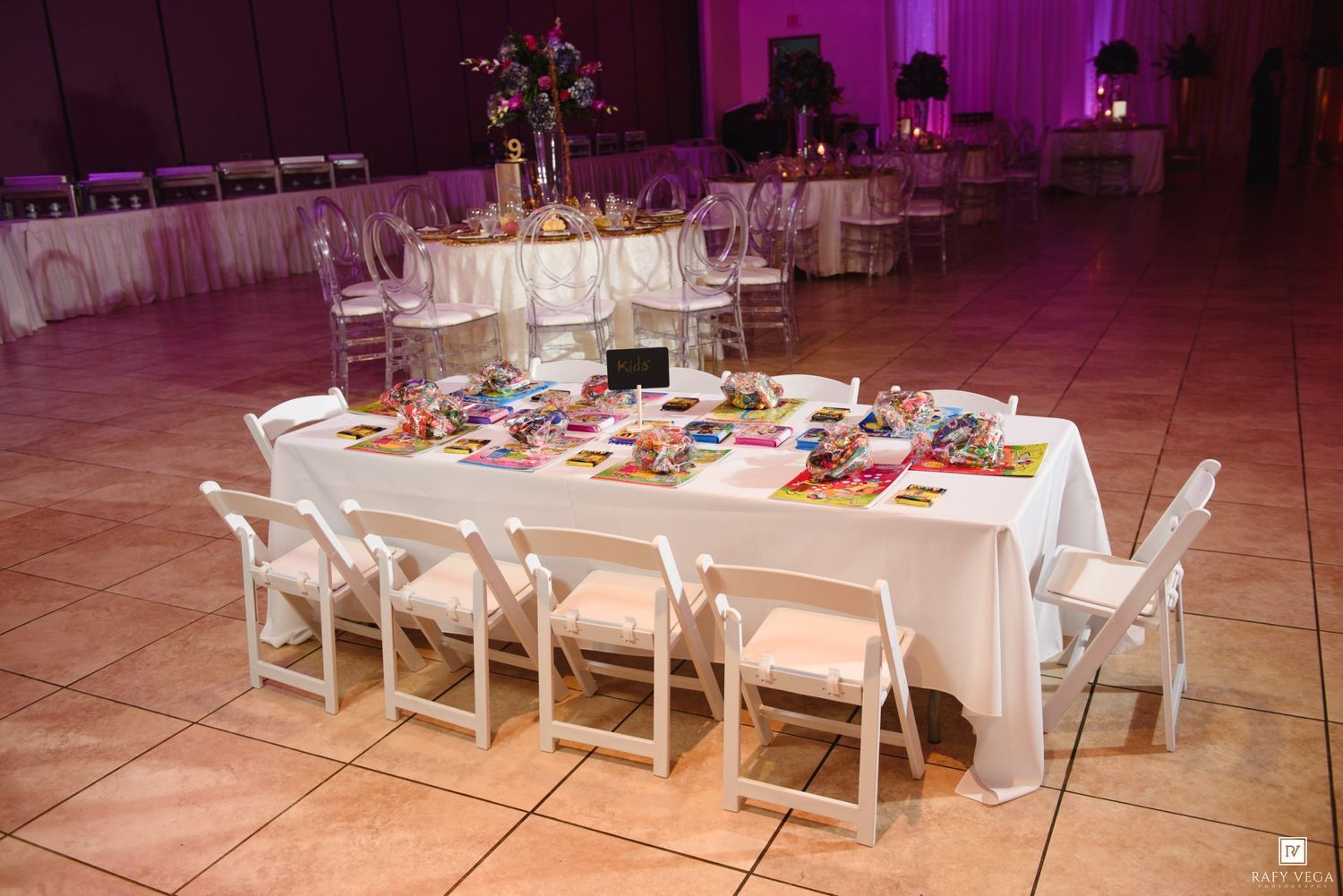 Elegant banquet hall with white-draped tables, chiavari chairs, and floral centerpieces on a dance floor with purple lighting.