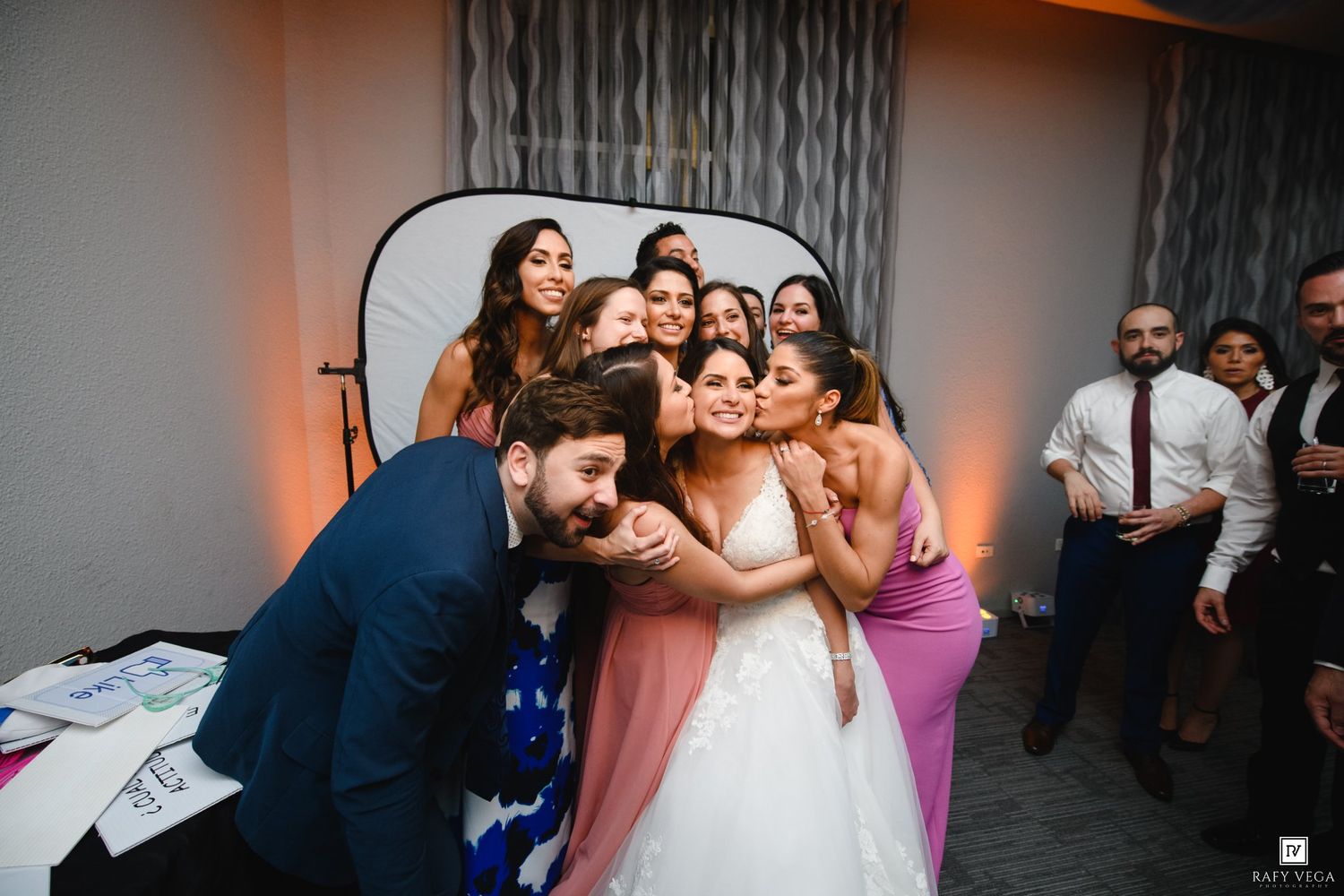 Bride posing with groom and bridesmaids at a fun wedding photo booth moment.