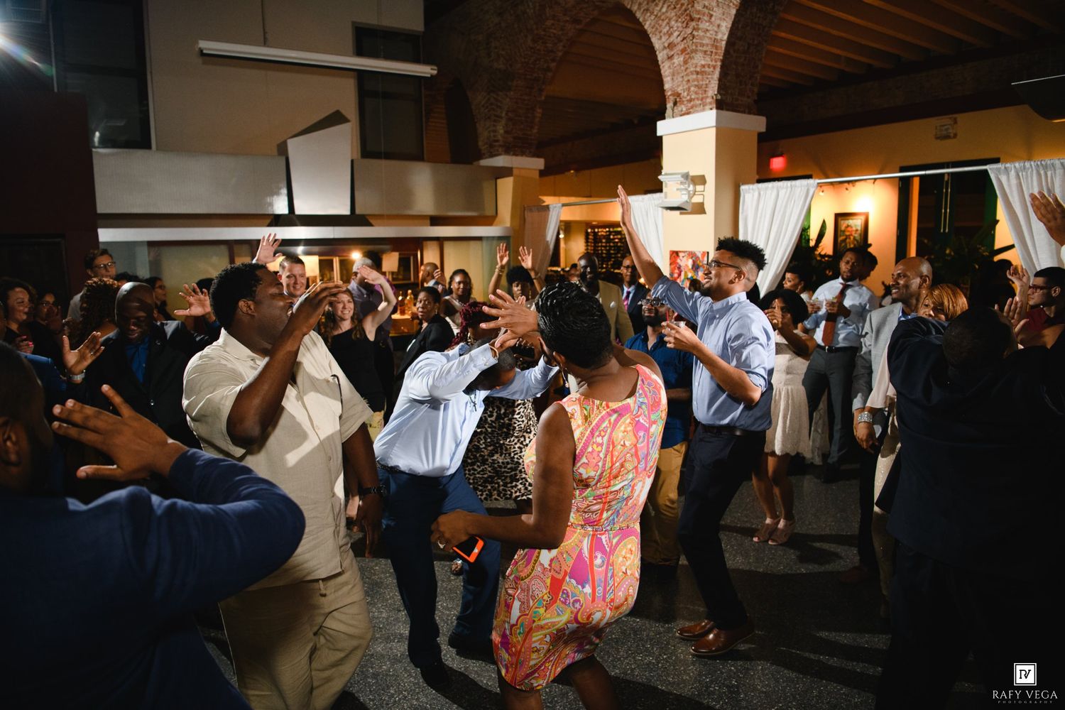Guests dancing and celebrating at an indoor wedding reception party in a warmly lit venue.