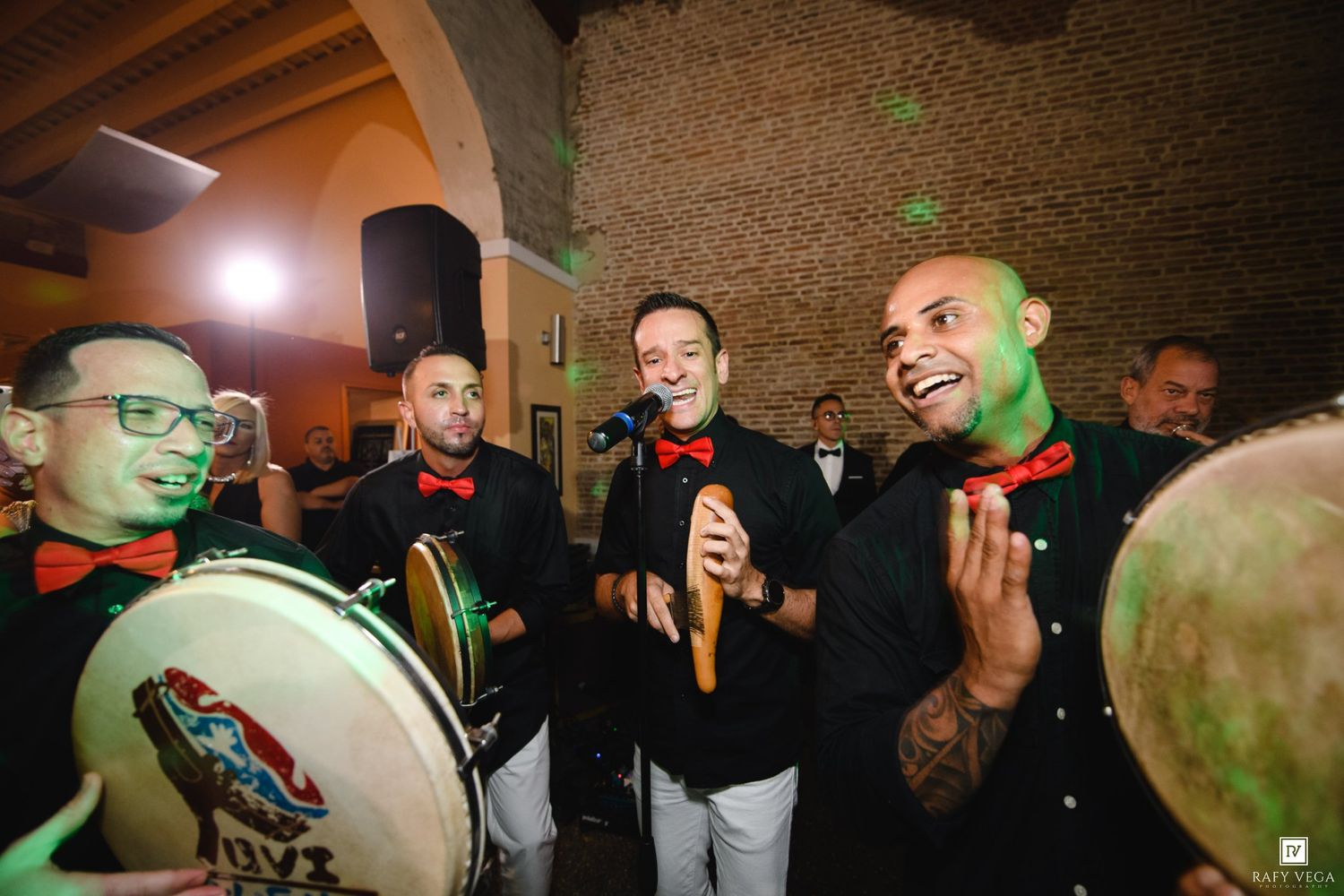 Live band performers in black uniforms playing drums and maracas at a festive event.