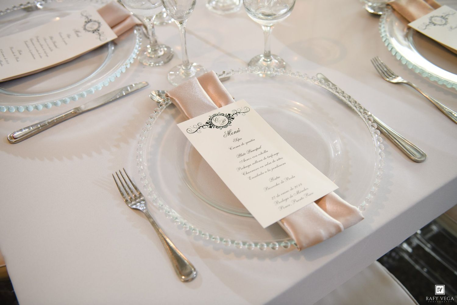 Elegant wedding reception place setting with blush ribbon and menu card on crystal charger plate.