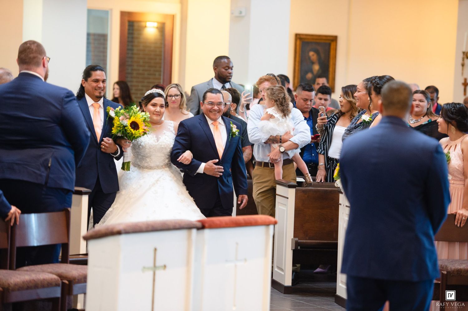 Bride in white gown walks down the aisle with her father at a church wedding ceremony.