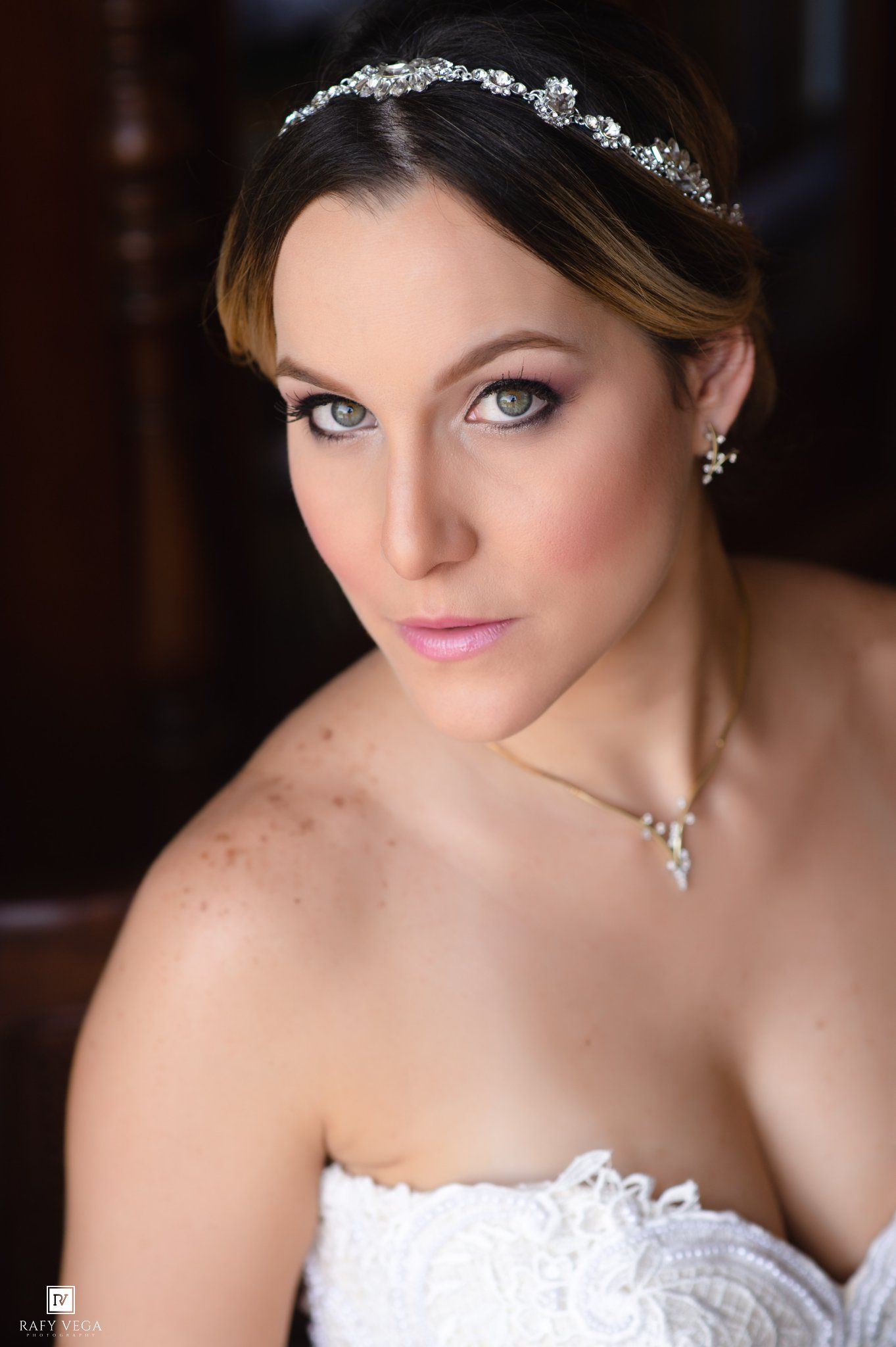 Elegant bride wearing a crystal headband, pearl earrings, and strapless lace gown with smoky eye makeup.