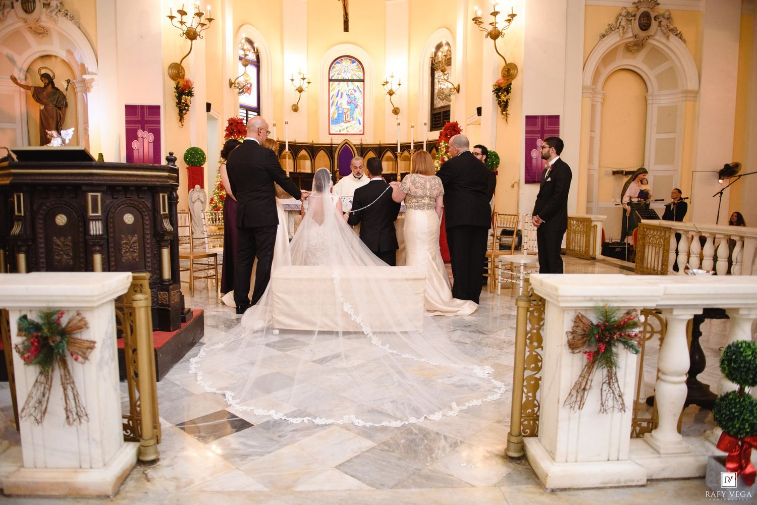 Bride and groom at church altar during wedding ceremony with elegant white veil and Christmas decorations.