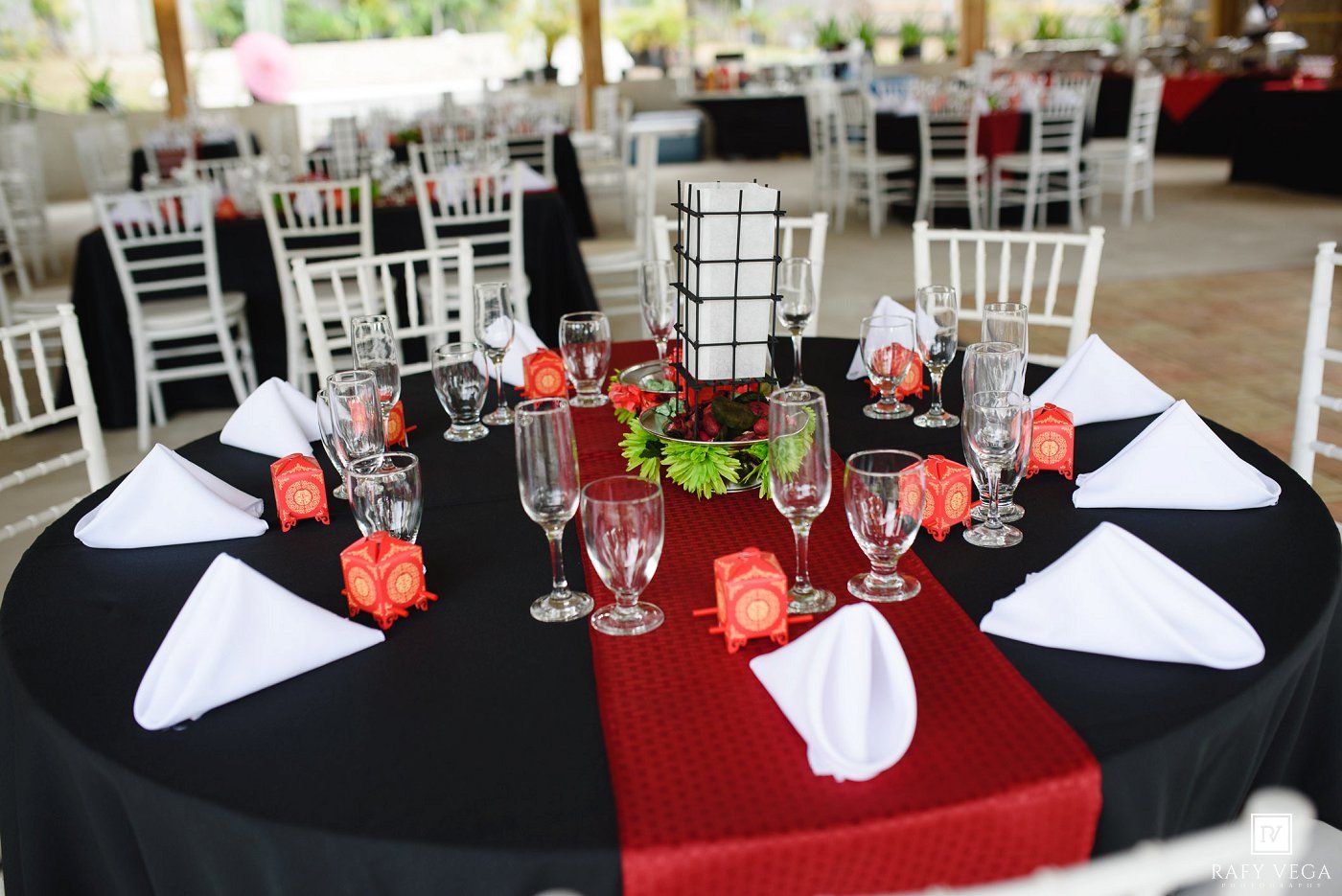 Elegant wedding reception table with black tablecloth, red runner, white napkins, and glassware.