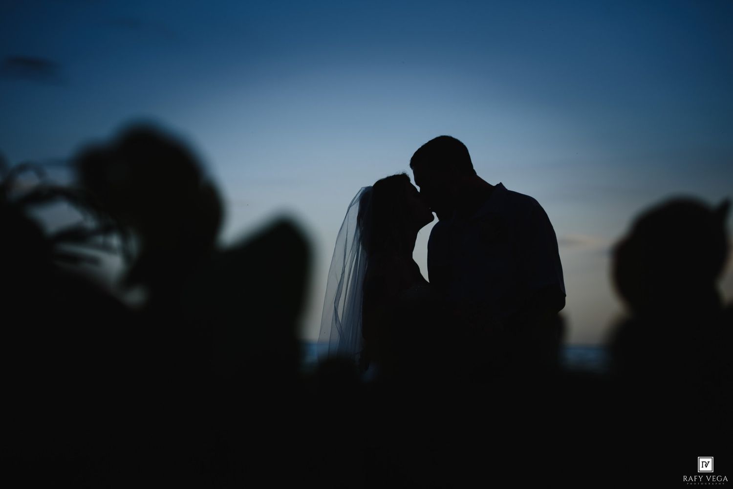 Silhouette of bride and groom sharing a kiss at dusk, with a beautiful blue twilight sky backdrop.