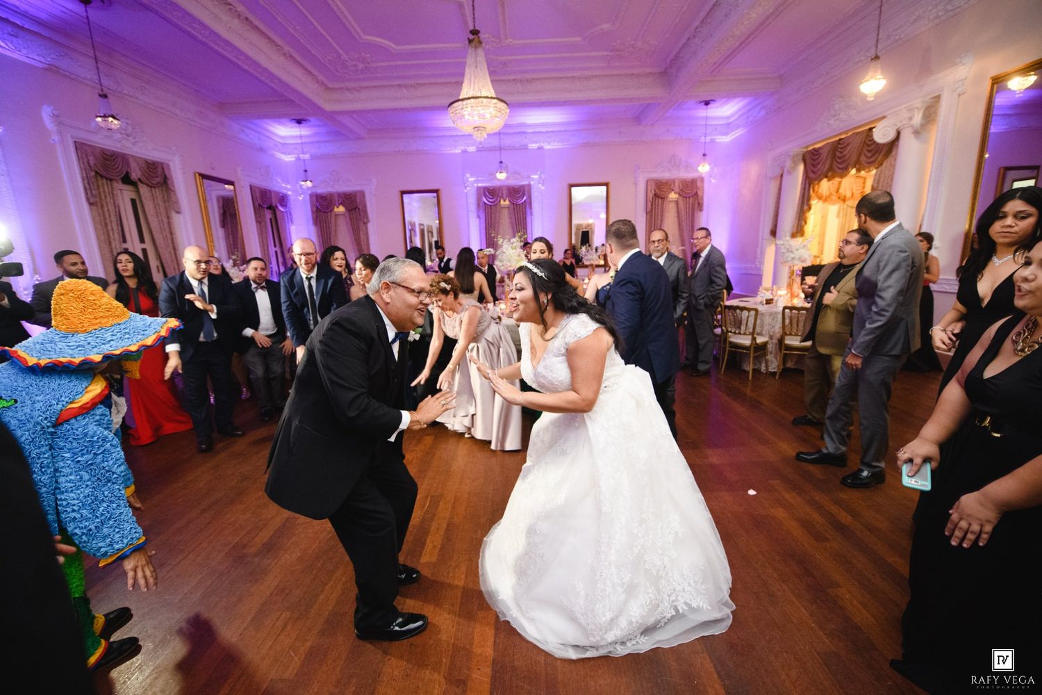 Bride and groom share a lively dance at their elegant wedding reception with guests watching in a grand ballroom.