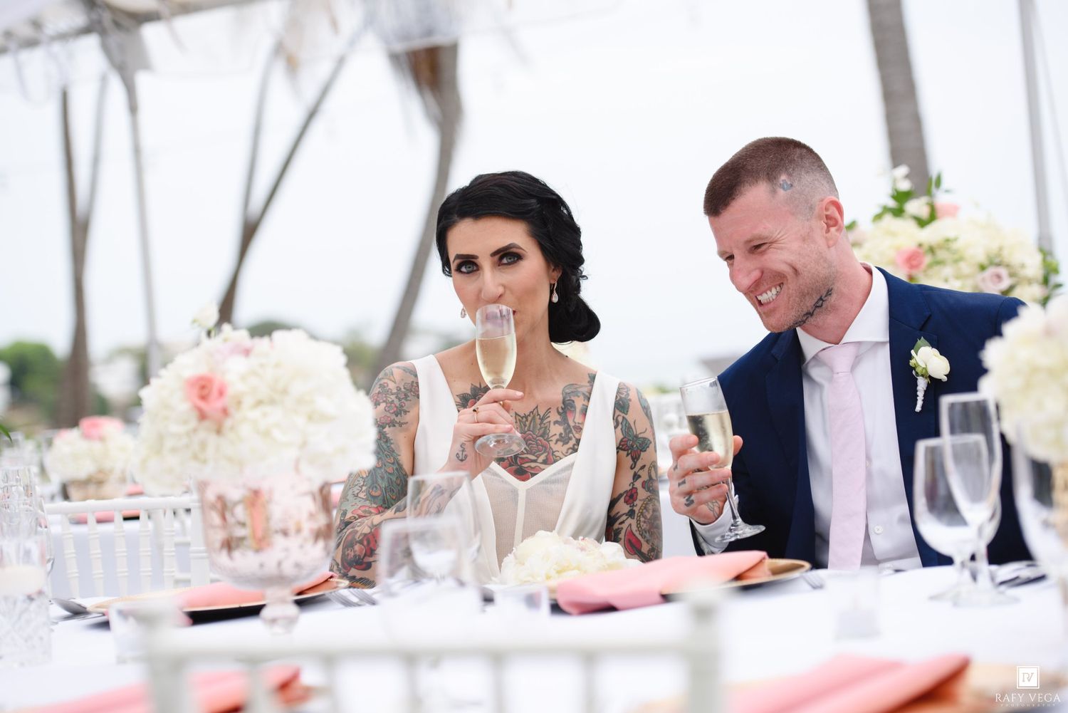 Bride and groom toasting with champagne at elegant outdoor wedding reception table with floral centerpieces.