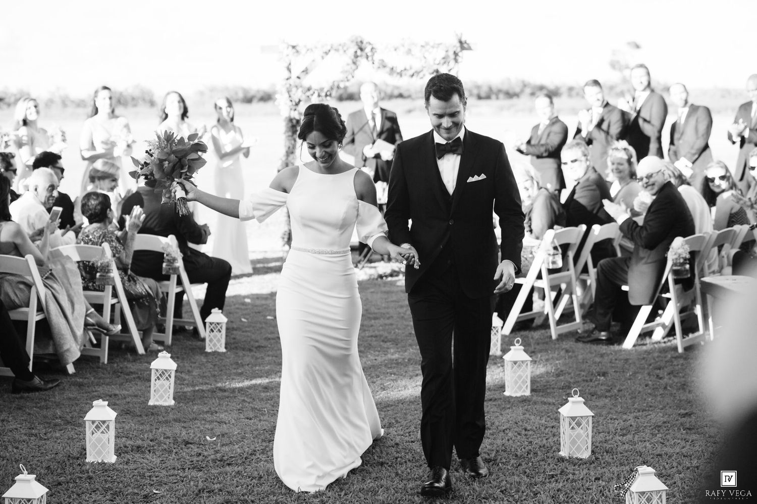 Black and white photo of a newlywed couple walking down the aisle at an outdoor wedding ceremony.