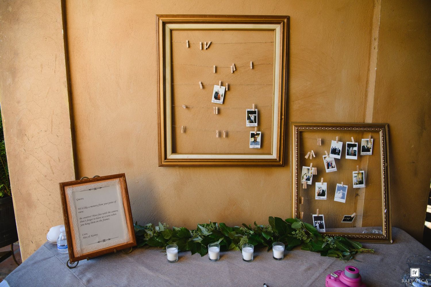 Gold-framed corkboards displaying Polaroid photos on a decorated table with greenery garlands and candles at a wedding reception.