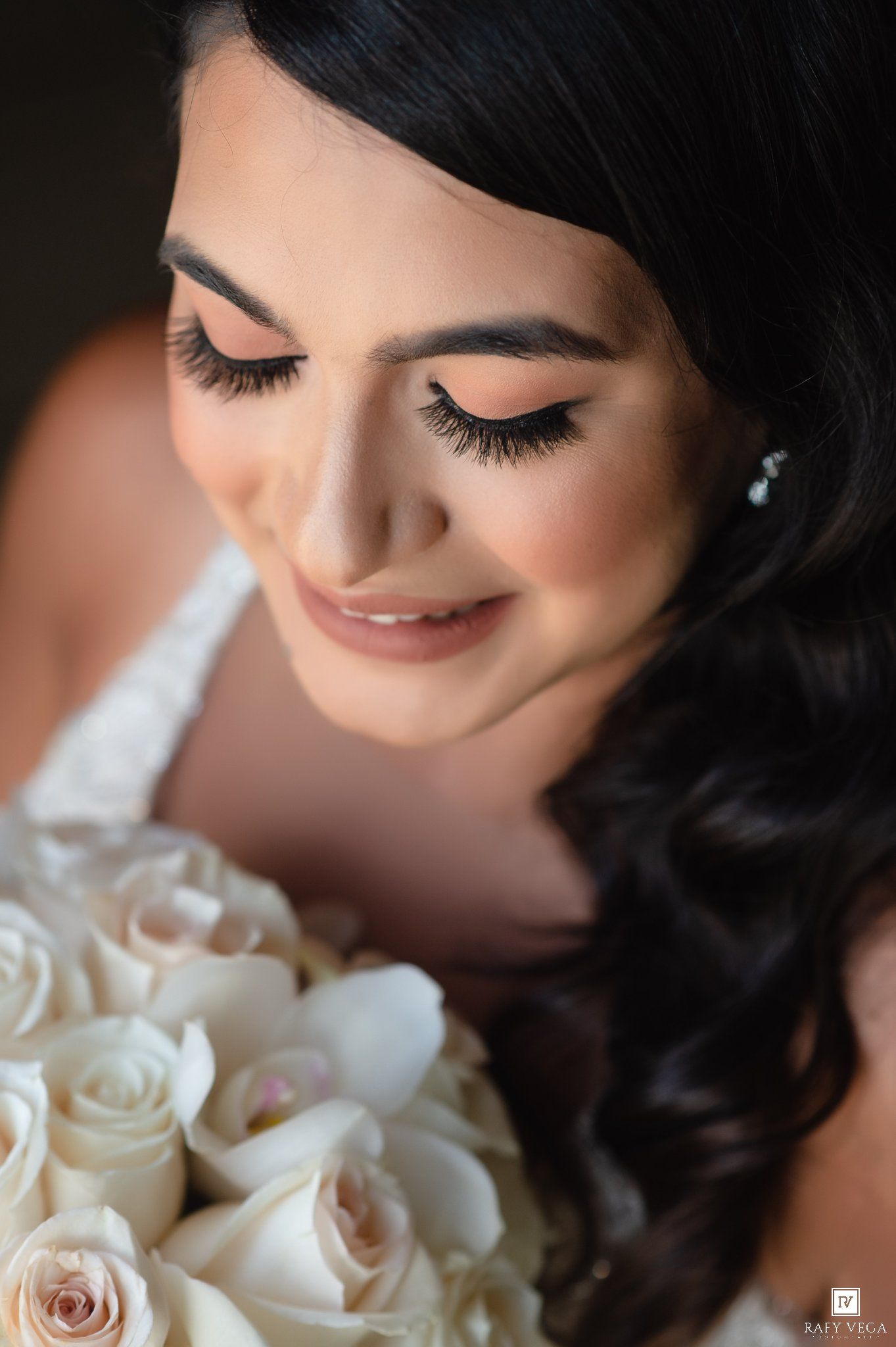 Bride with dramatic lashes and soft glam makeup holds a white rose bouquet on her wedding day.