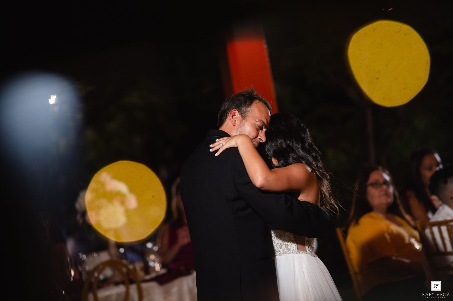 Bride and groom share their first dance under golden bokeh lights at an outdoor evening wedding reception.