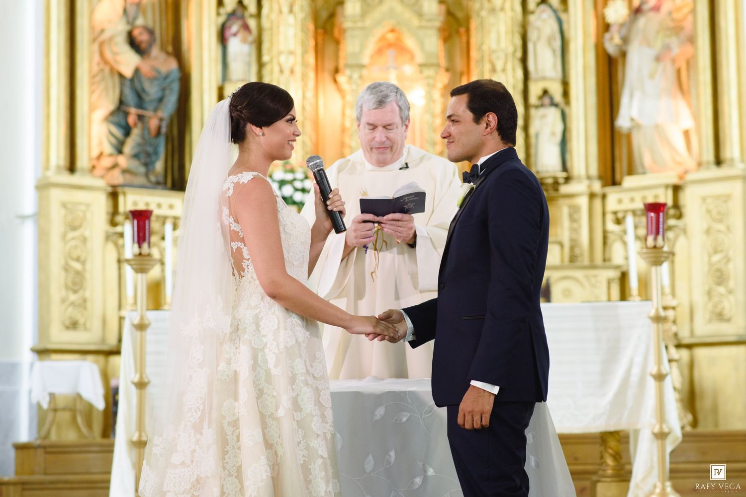 Bride and groom exchange vows at ornate golden church altar with officiant during wedding ceremony.