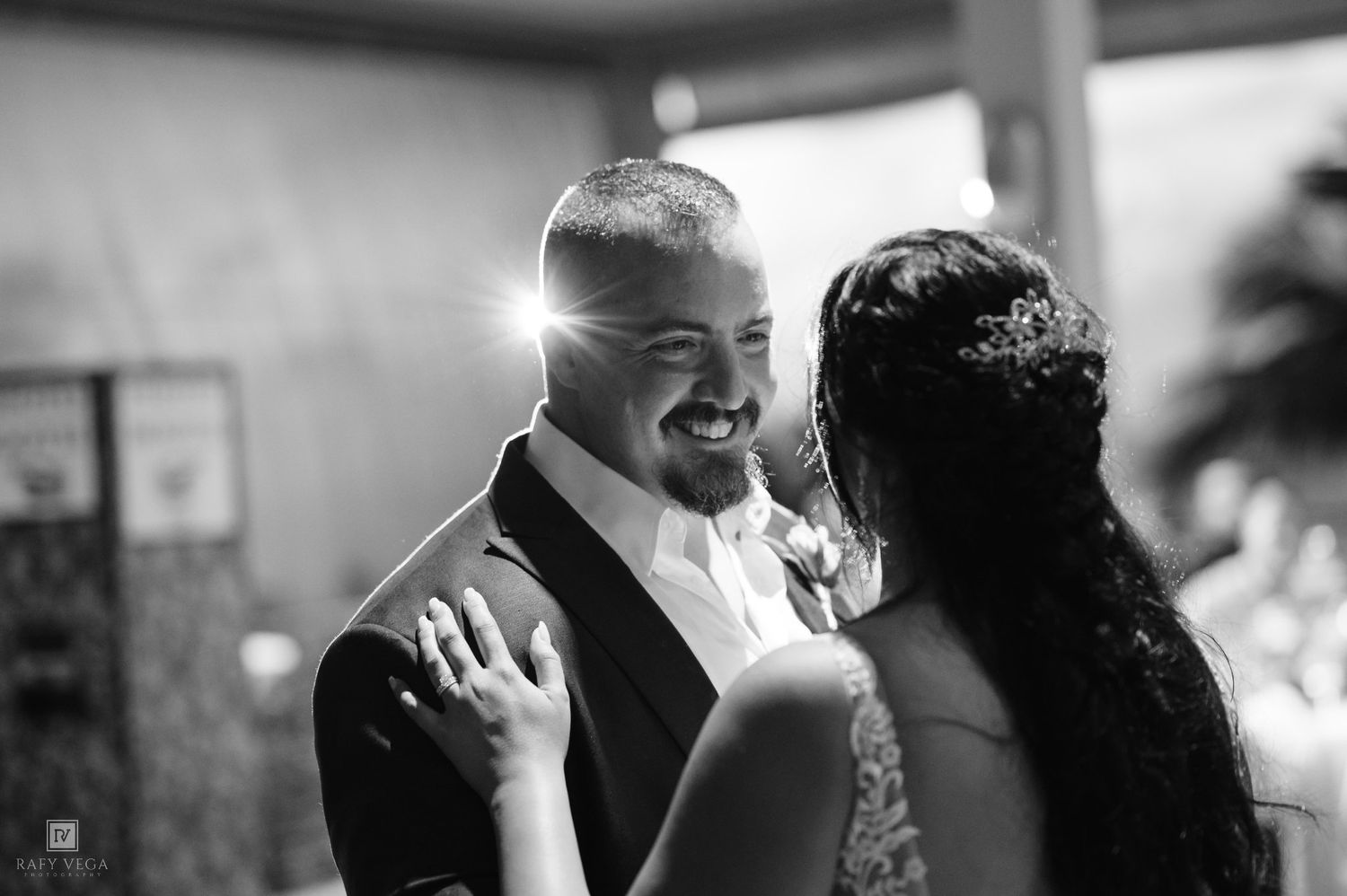 Black and white photo of a smiling groom sharing a first dance with his bride at a wedding reception.