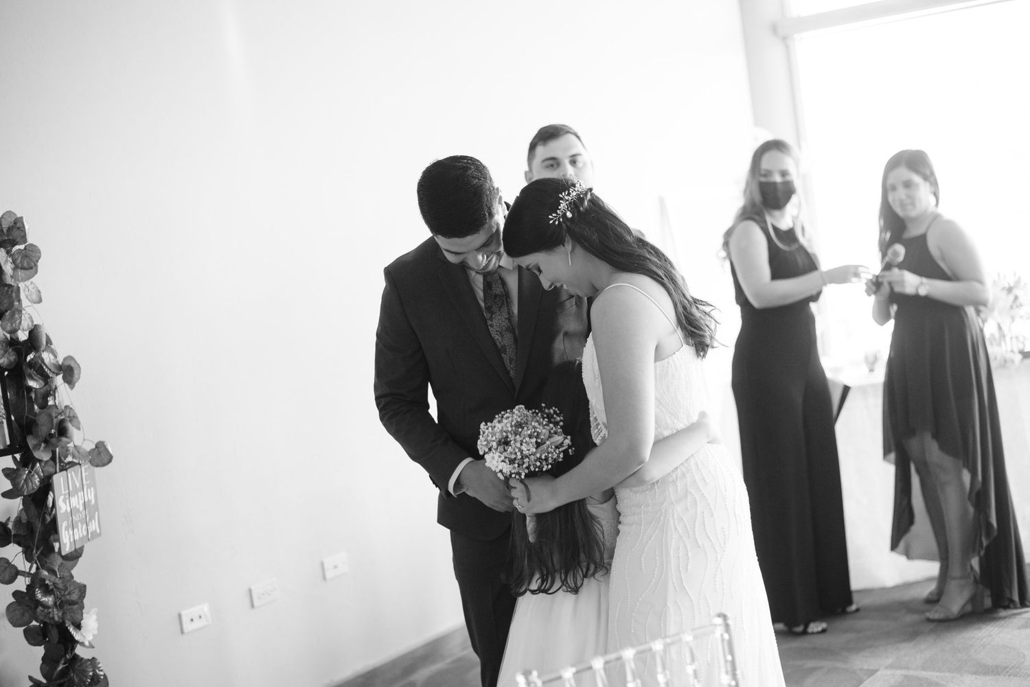 Black and white wedding photo of bride and groom sharing a kiss during ceremony with bridesmaids in background.
