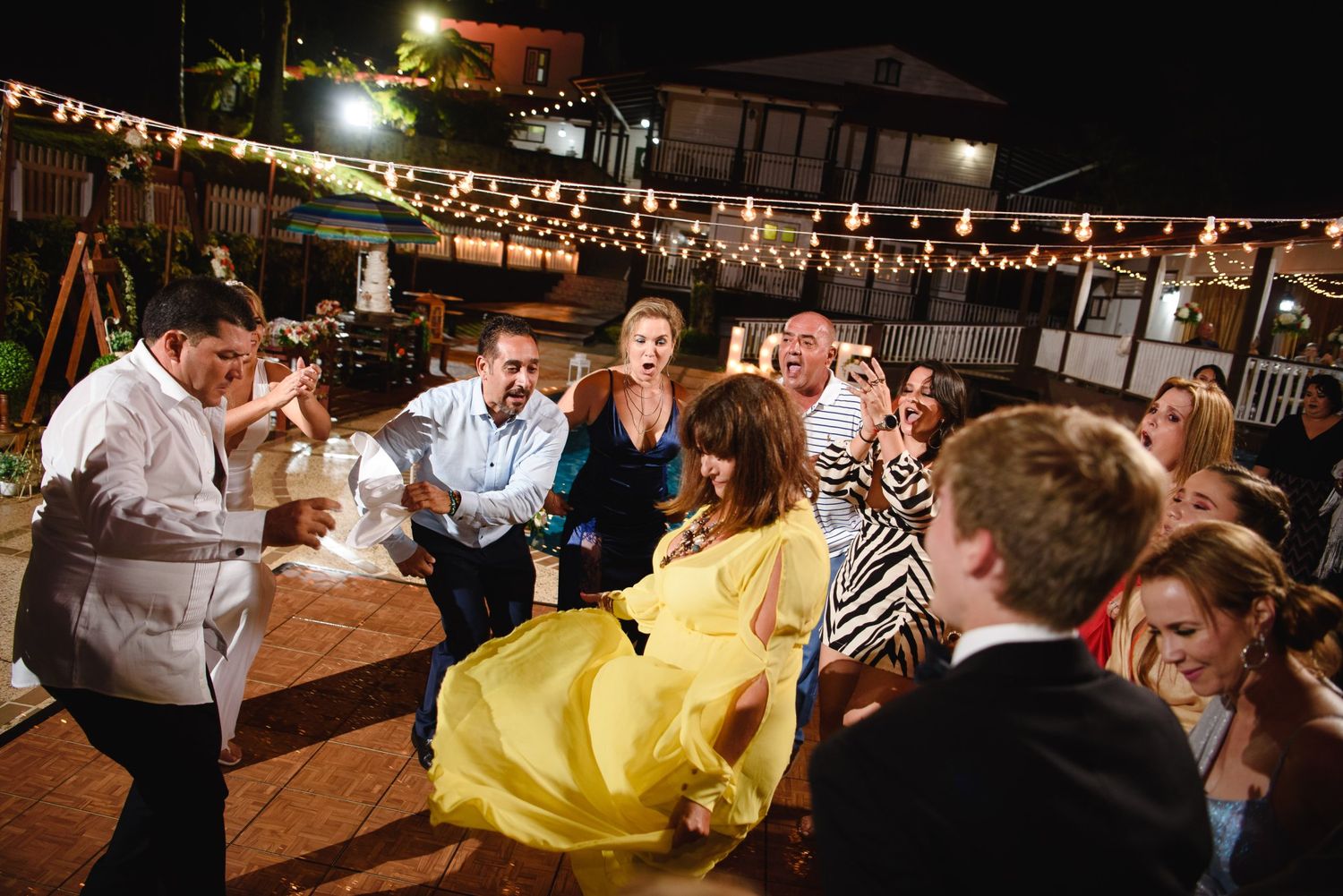 Guests dancing energetically at an outdoor wedding reception under string lights at night.
