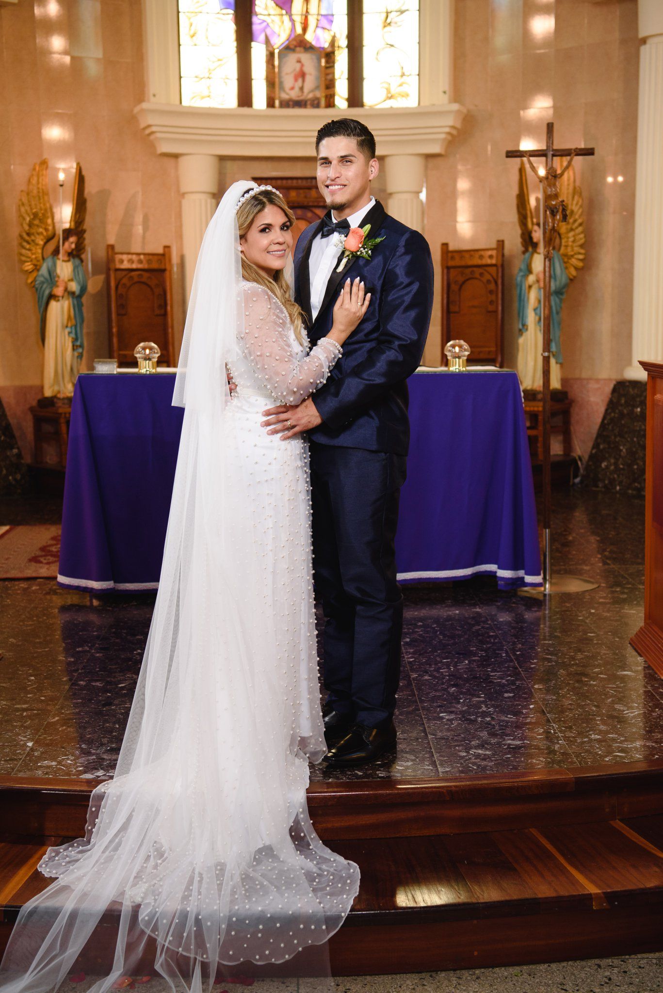 Bride and groom posing together in a church after their wedding ceremony, bride in white gown with veil.
