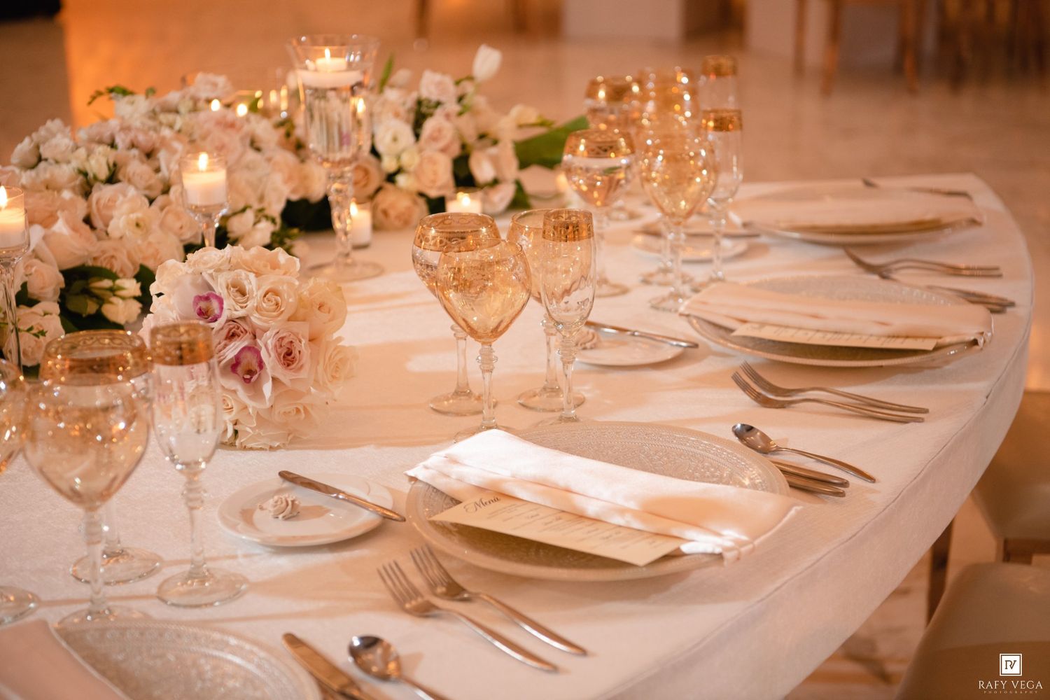 Elegant wedding reception table set with crystal glasses, gold cutlery, white linens, and floral centerpieces.