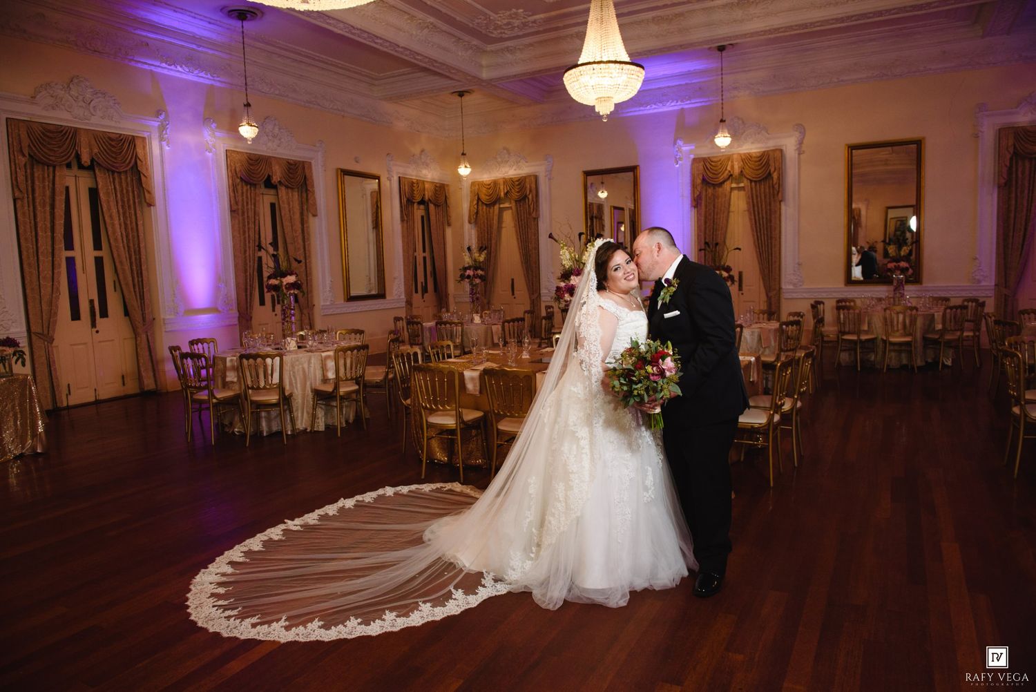 Bride and groom share a romantic moment on the dance floor of an elegant ballroom with purple uplighting.