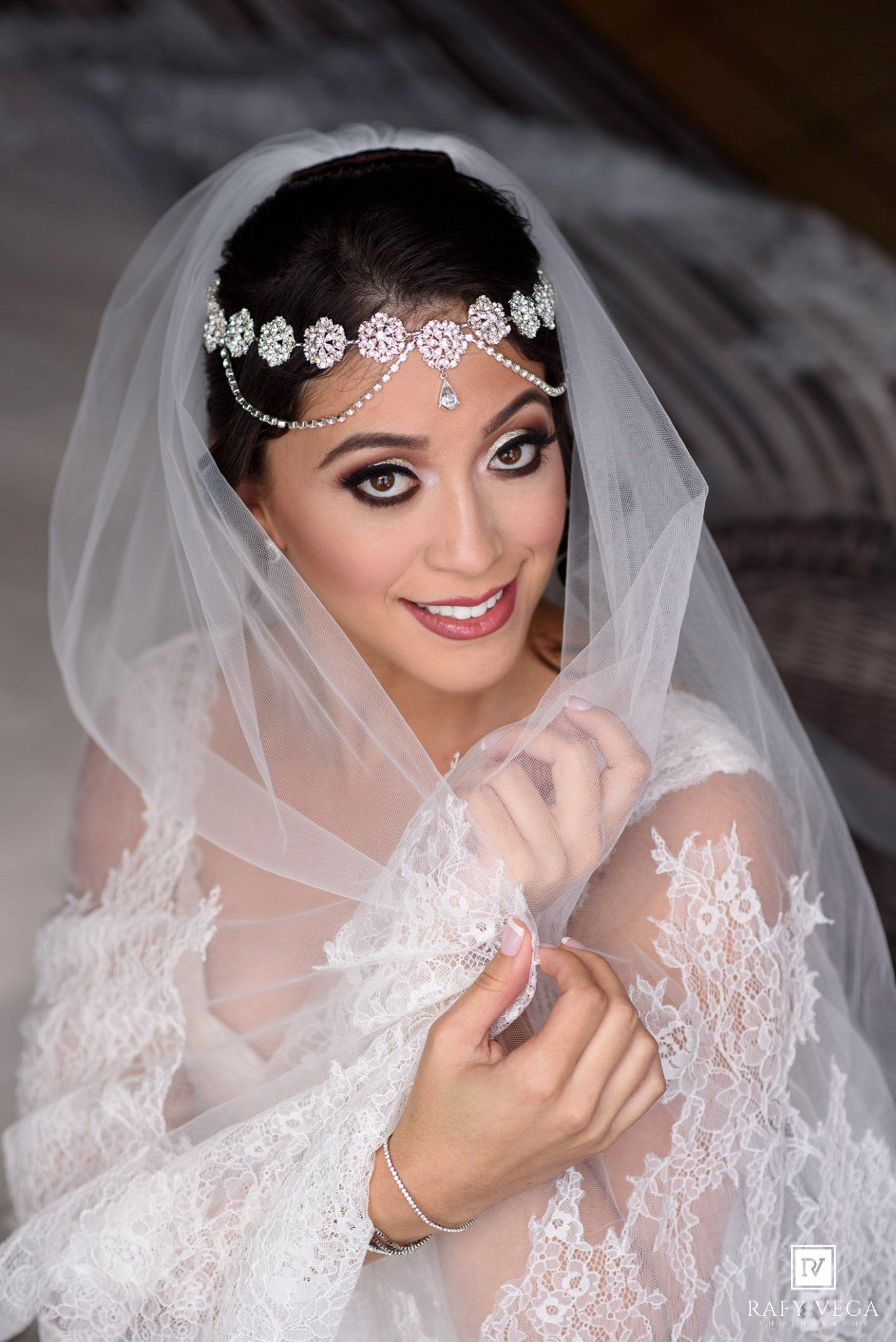 Elegant bride wearing lace wedding dress, crystal headpiece, and veil, smiling beautifully on her wedding day.