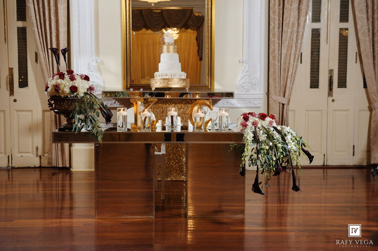 Elegant wedding reception setup with white tiered cake, floral arrangements, and candles on a wooden sweetheart table.