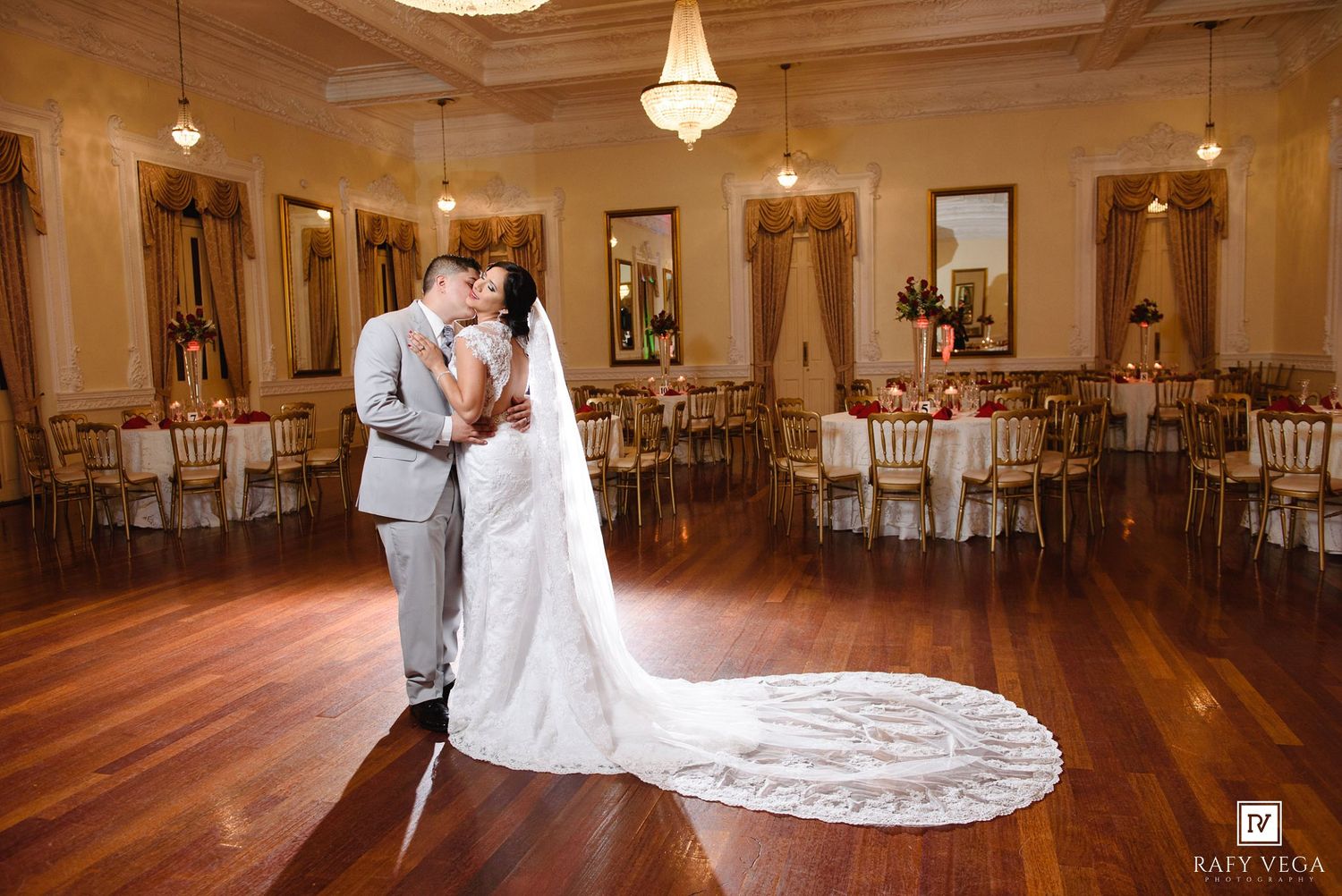 Bride and groom share a romantic kiss on the dance floor of an elegant wedding venue with gold chairs and floral decor.