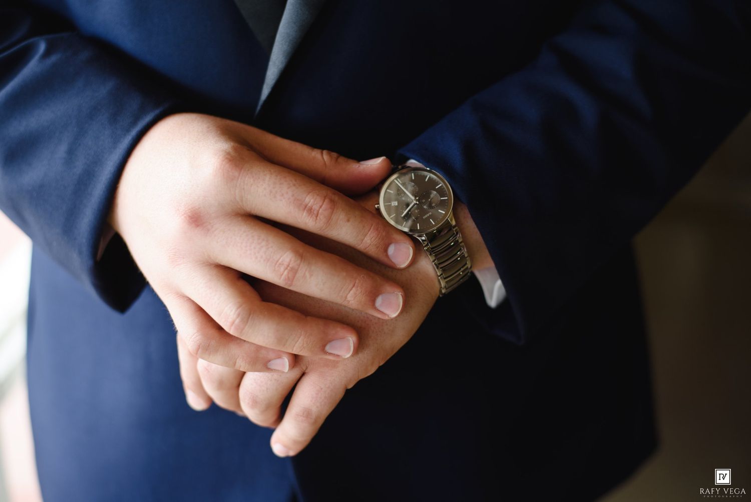 Close-up of groom adjusting classic gold watch on wrist wearing navy blue suit.