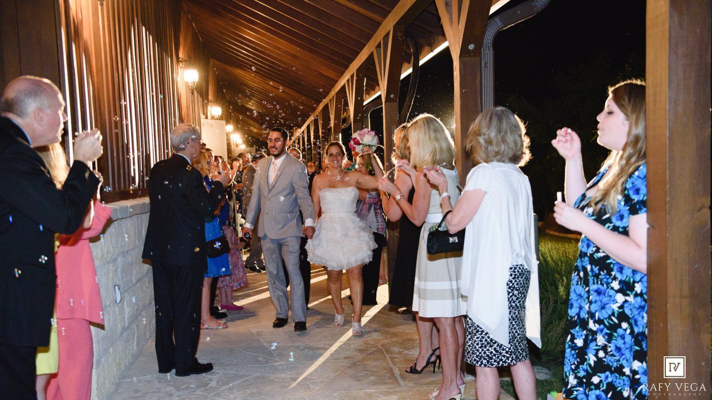 Bride and groom exit wedding reception as guests celebrate and applaud along the pathway.