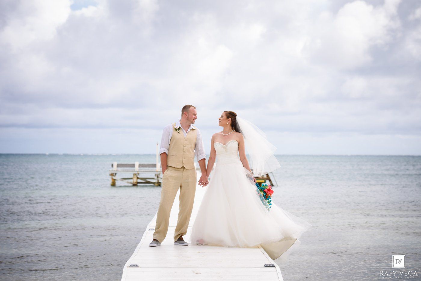Bride and groom holding hands on a white dock overlooking the ocean on their tropical beach wedding day.