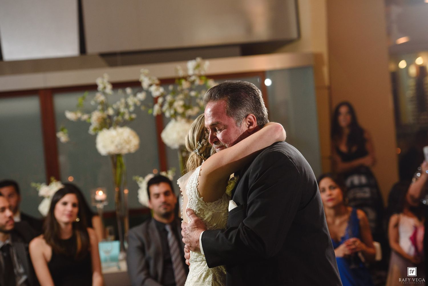 Bride and groom share an emotional first dance embrace surrounded by wedding guests at their reception.