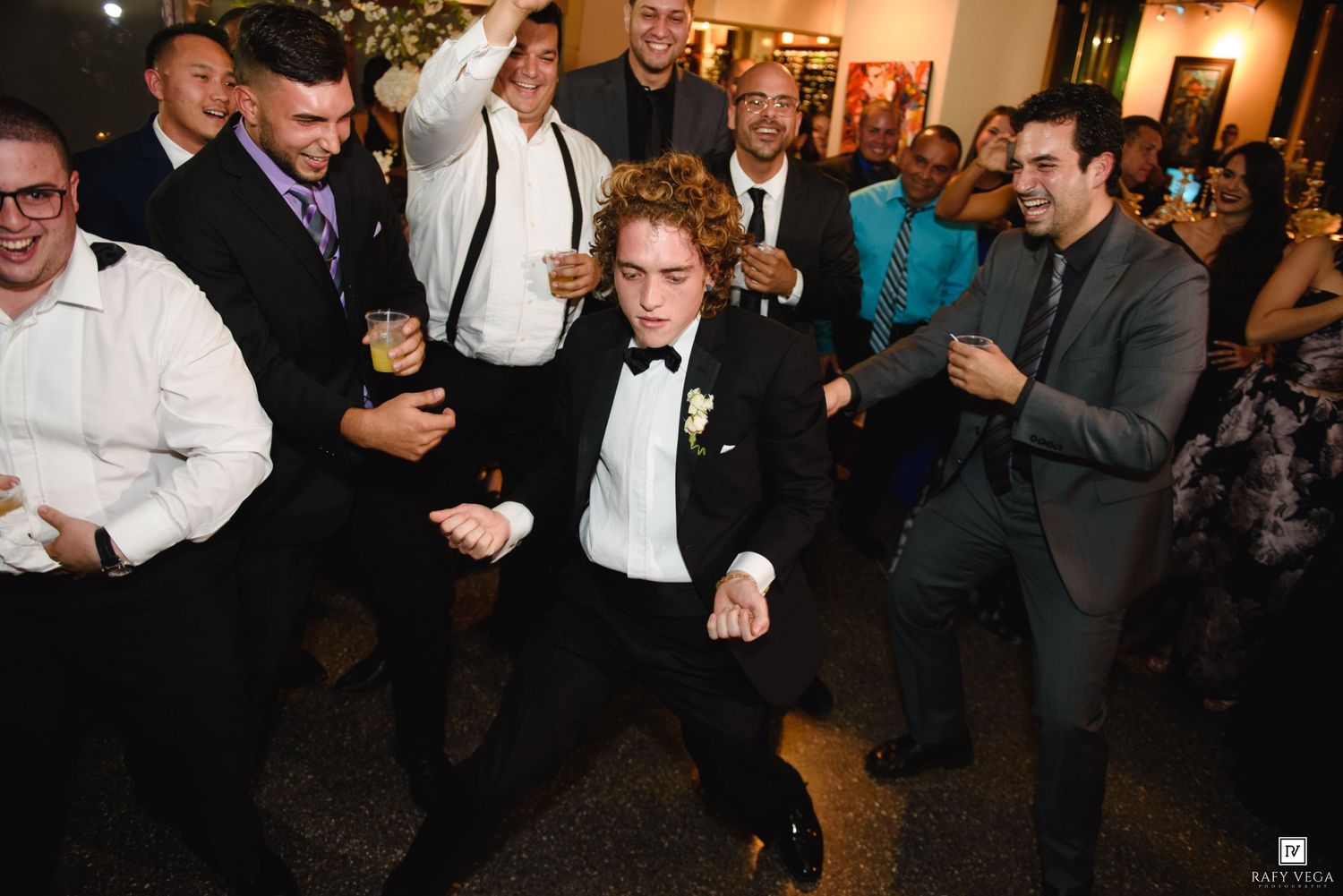 Groom dances energetically with groomsmen and guests at wedding reception.