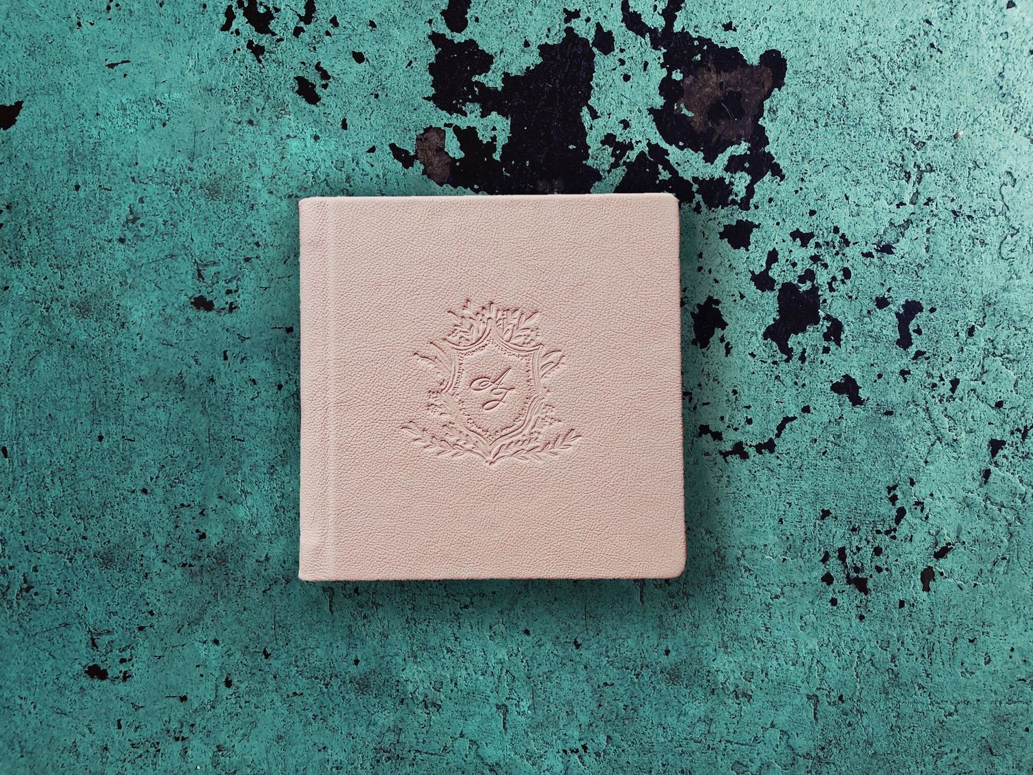 Elegant embossed leather journal with floral crest design on teal distressed surface.