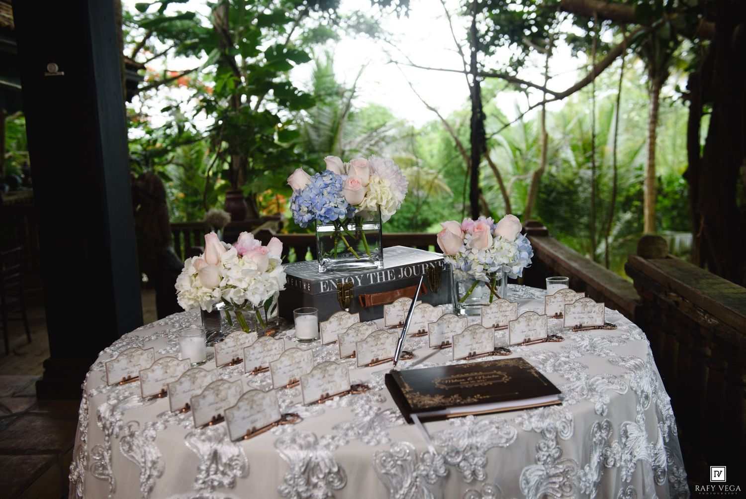 Elegant outdoor wedding escort card table with white lace cloth, floral arrangements, and place cards in a garden setting.