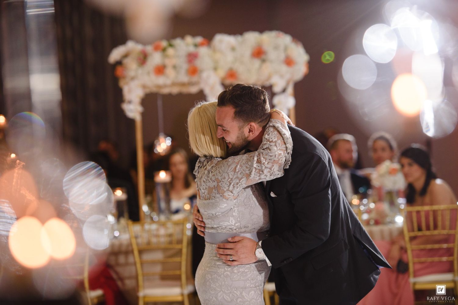 Bride and groom share a romantic first dance embrace at elegant wedding reception with floral arrangements.