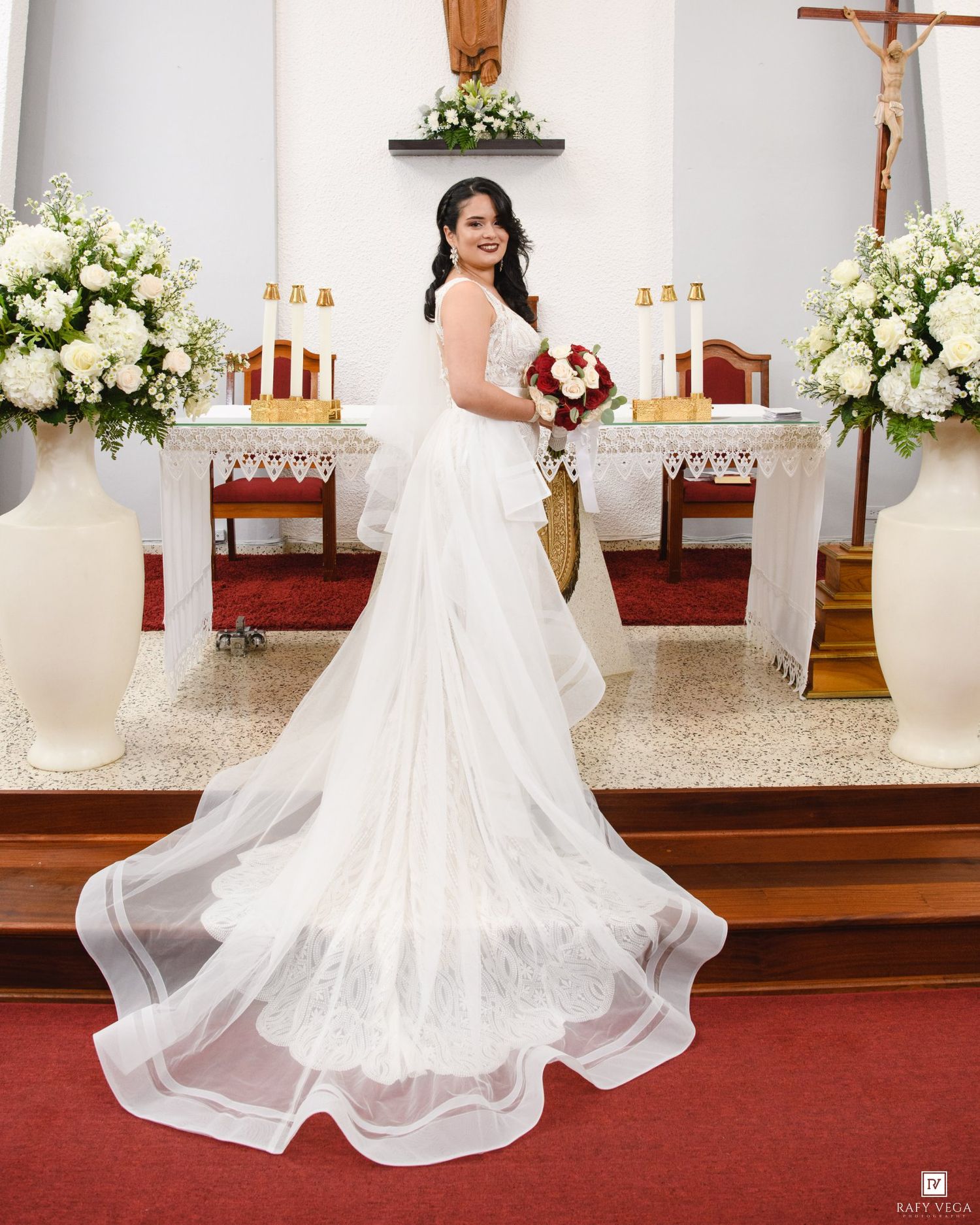 Elegant bride in white ball gown with long train holds bouquet at church altar.