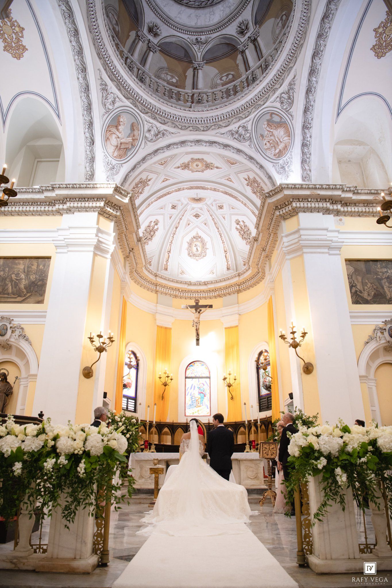 Bride and groom at altar of stunning baroque church with white floral arrangements.