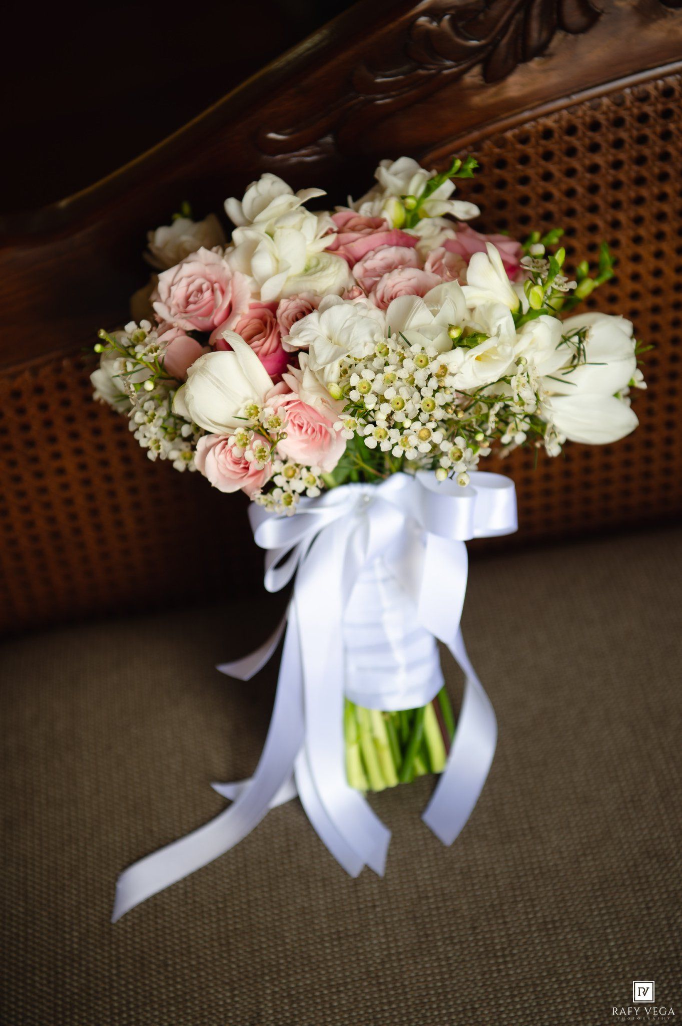 Elegant bridal bouquet of pink roses, white tulips, and small daisies tied with a white satin ribbon.