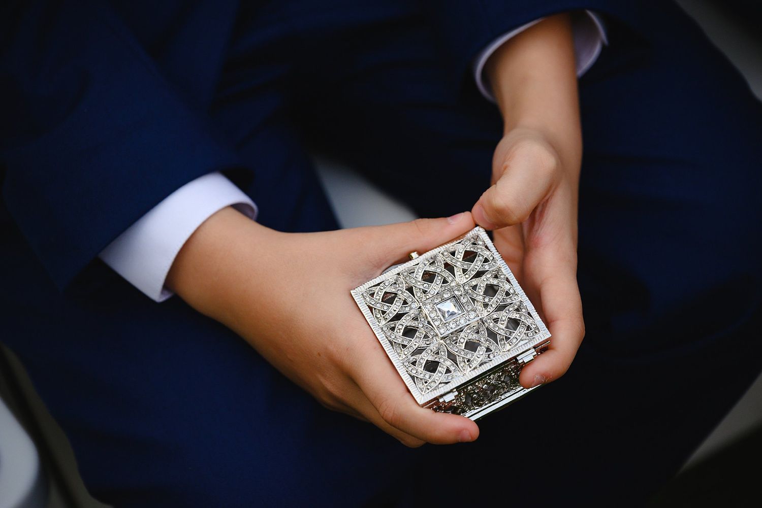 Person in blue suit holding ornate silver decorative box with intricate lattice design at a formal event.