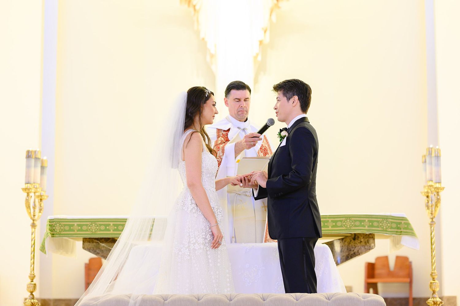 Bride and groom exchanging vows at a church altar with an officiant during a formal wedding ceremony.