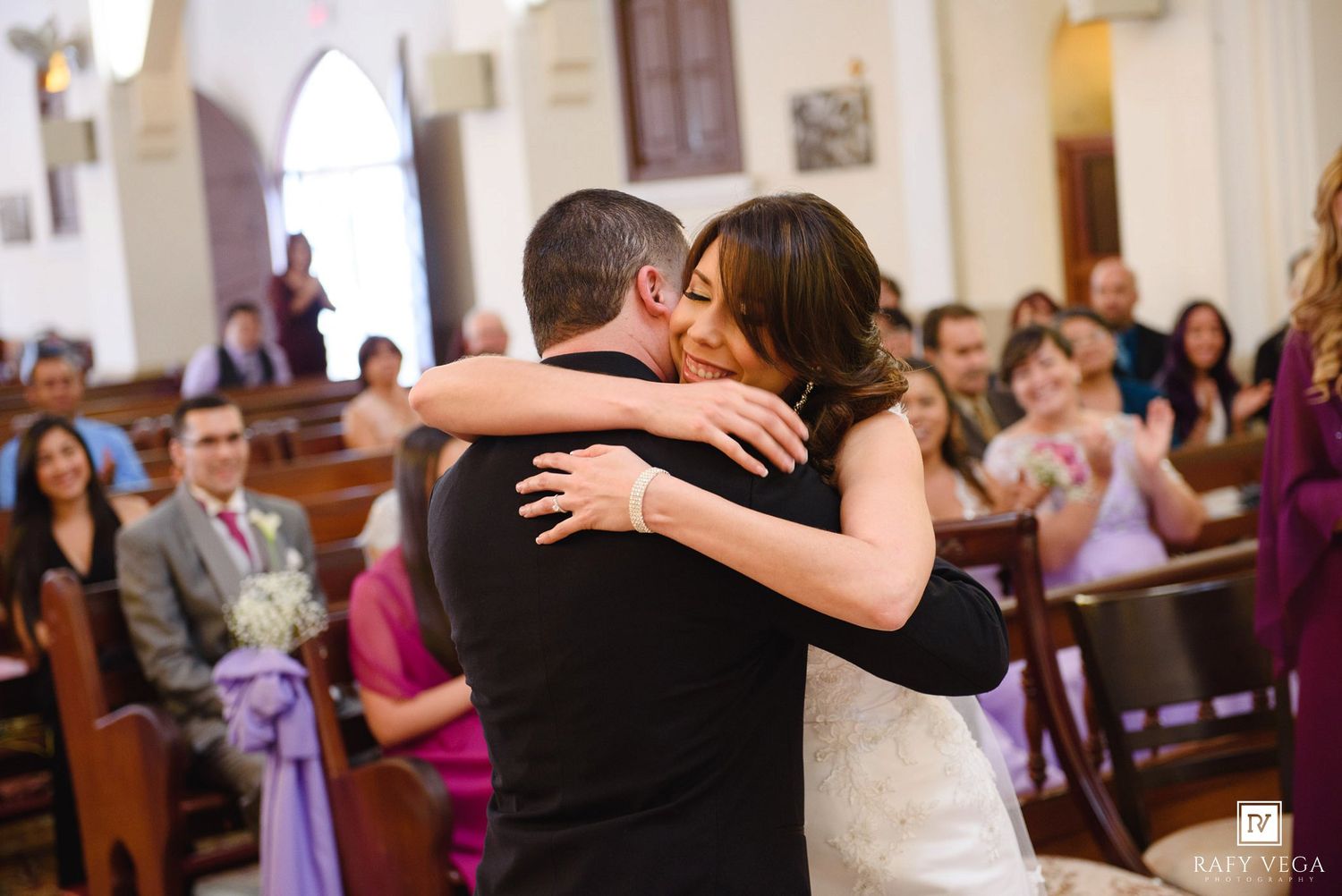 Bride and groom share emotional first hug after wedding ceremony at church altar.