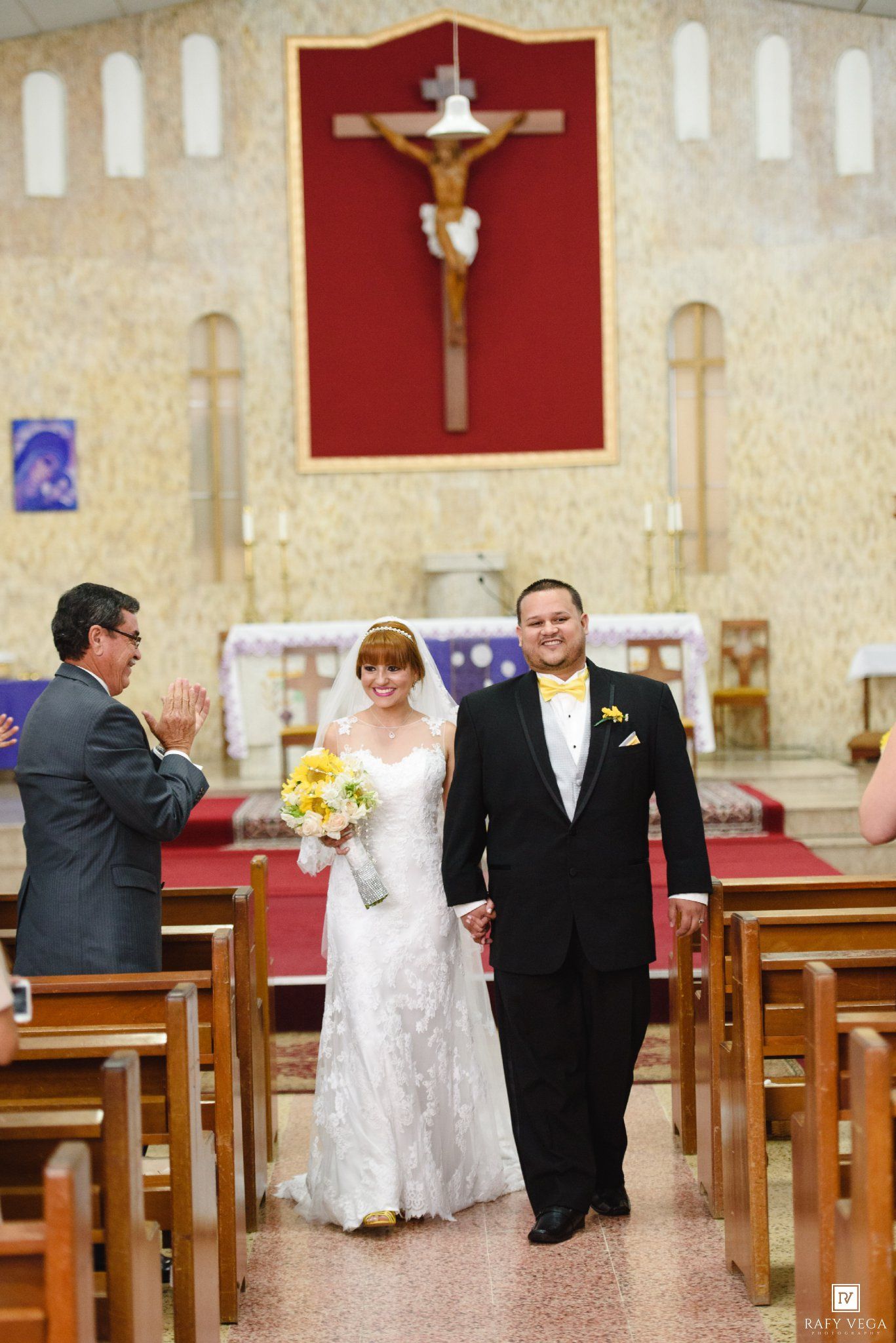 Bride and groom walking down church aisle after wedding ceremony, bride holding yellow sunflower bouquet.