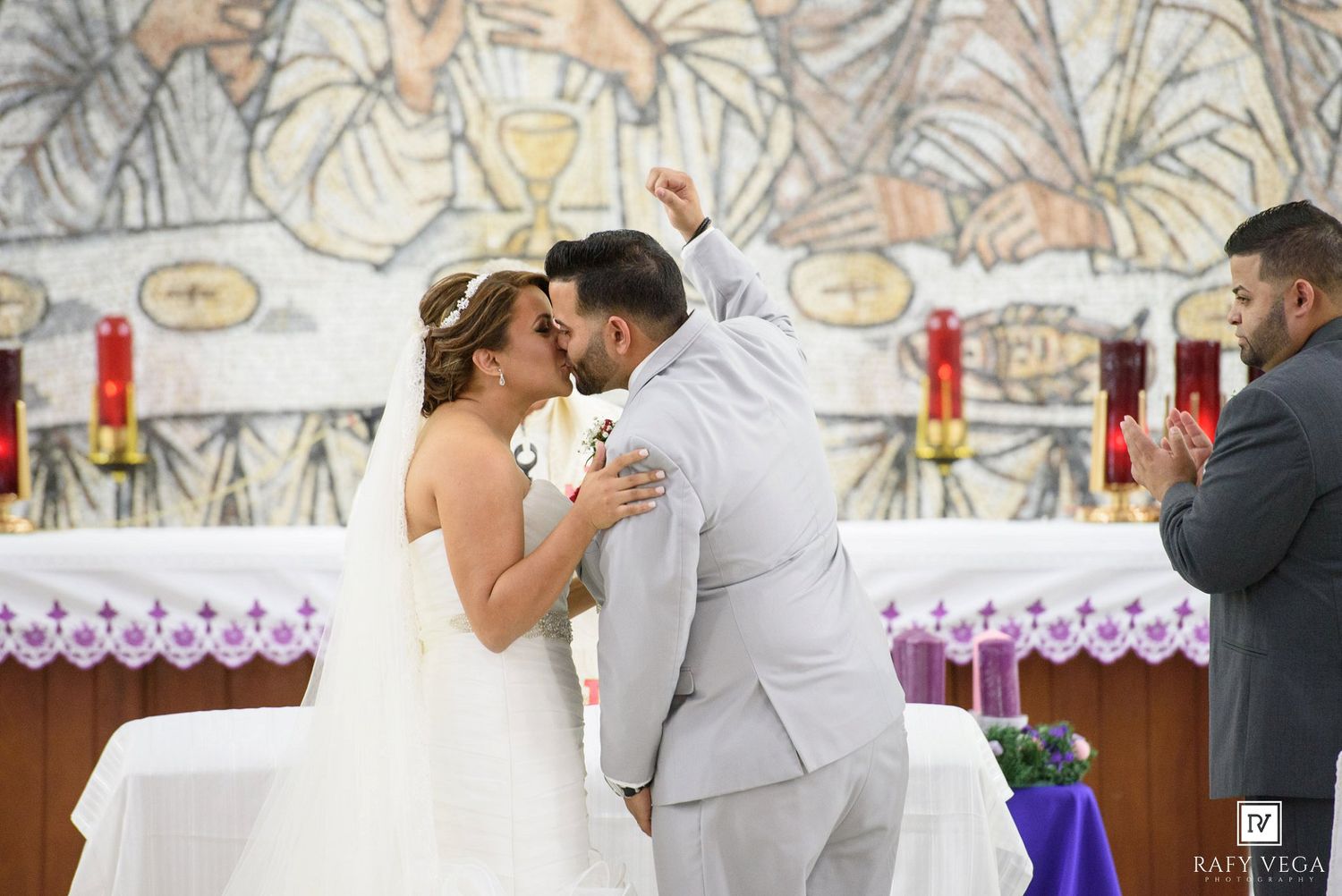 Bride and groom share first kiss at church altar as officiant celebrates behind them.