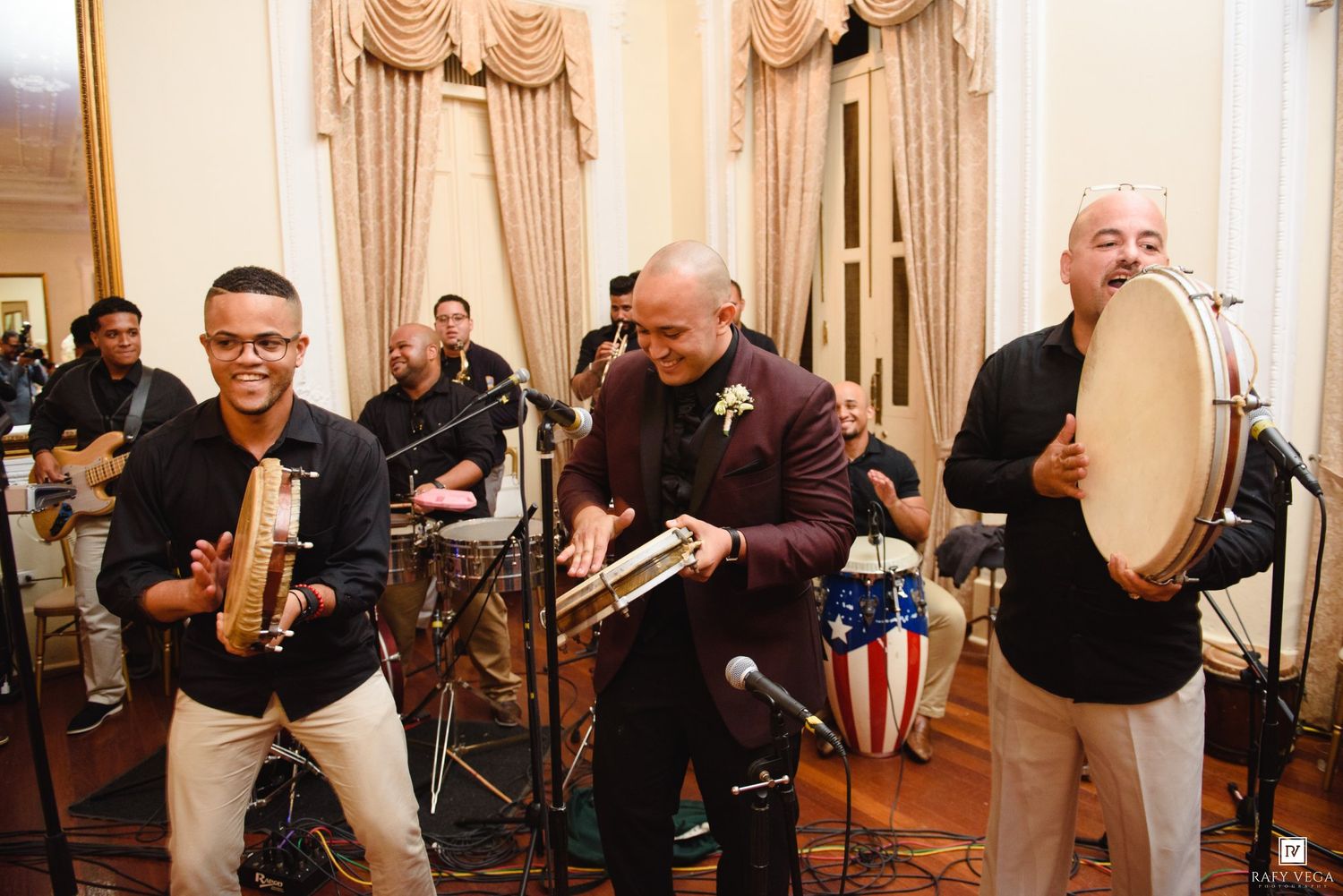 Latin band performing live at elegant event, playing percussion instruments including bongo and conga drums in formal venue.