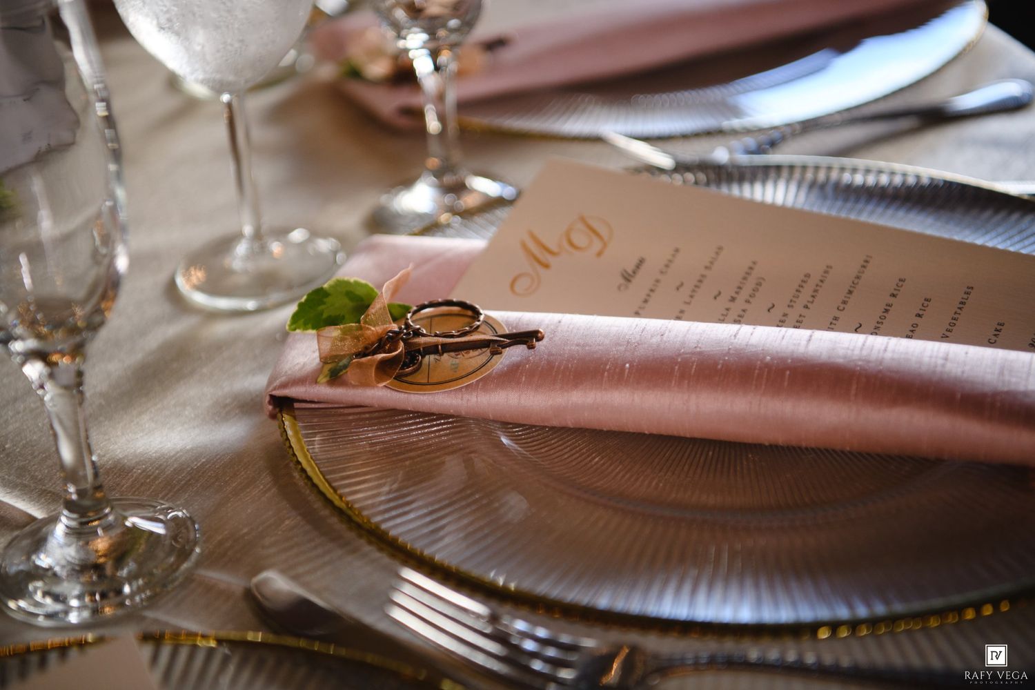 Close-up of a wedding place setting with pink napkin, gold-rimmed charger plate, and decorative ring holder.